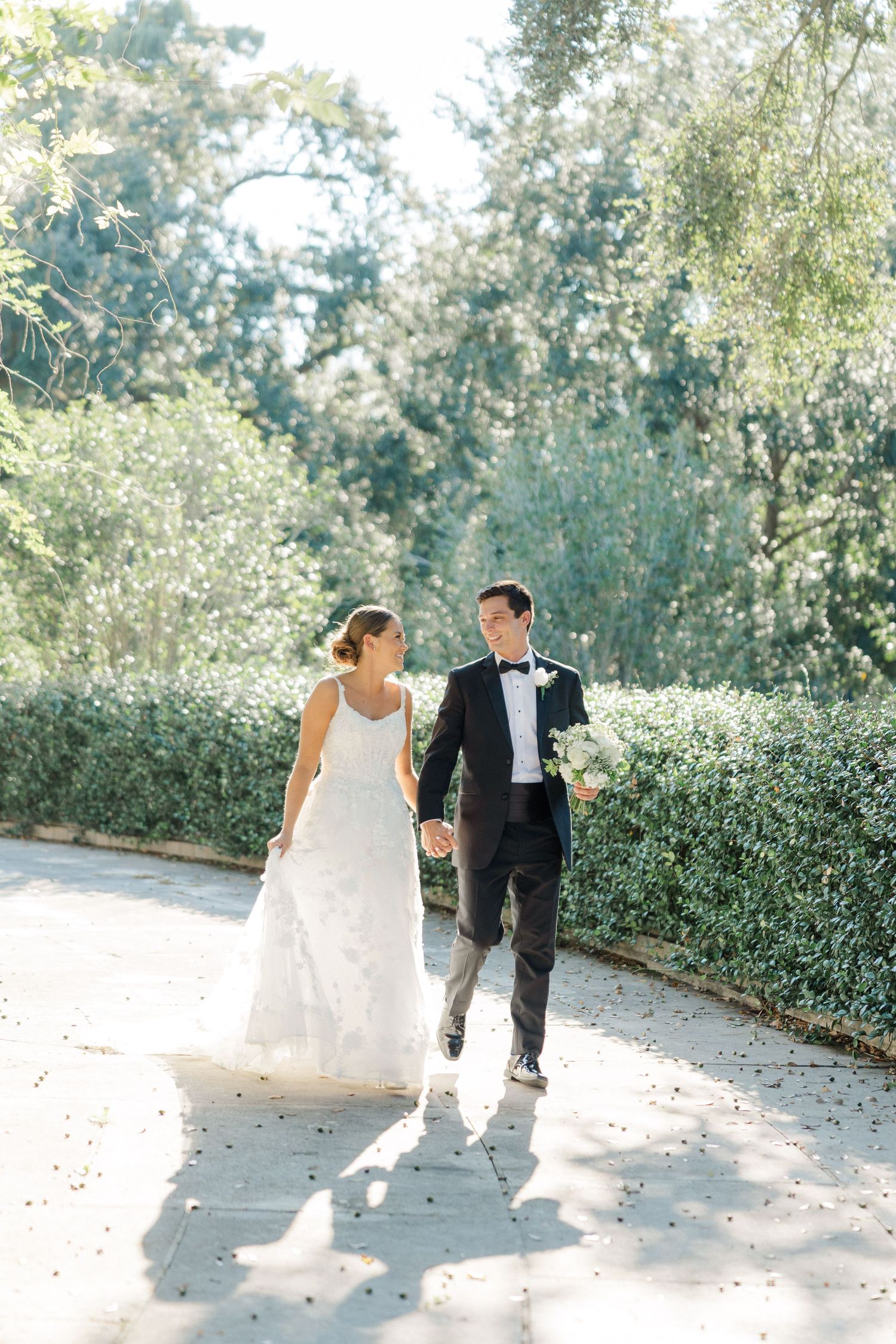 A couple strolls along a garden path surrounded by lush greenery on their wedding day.