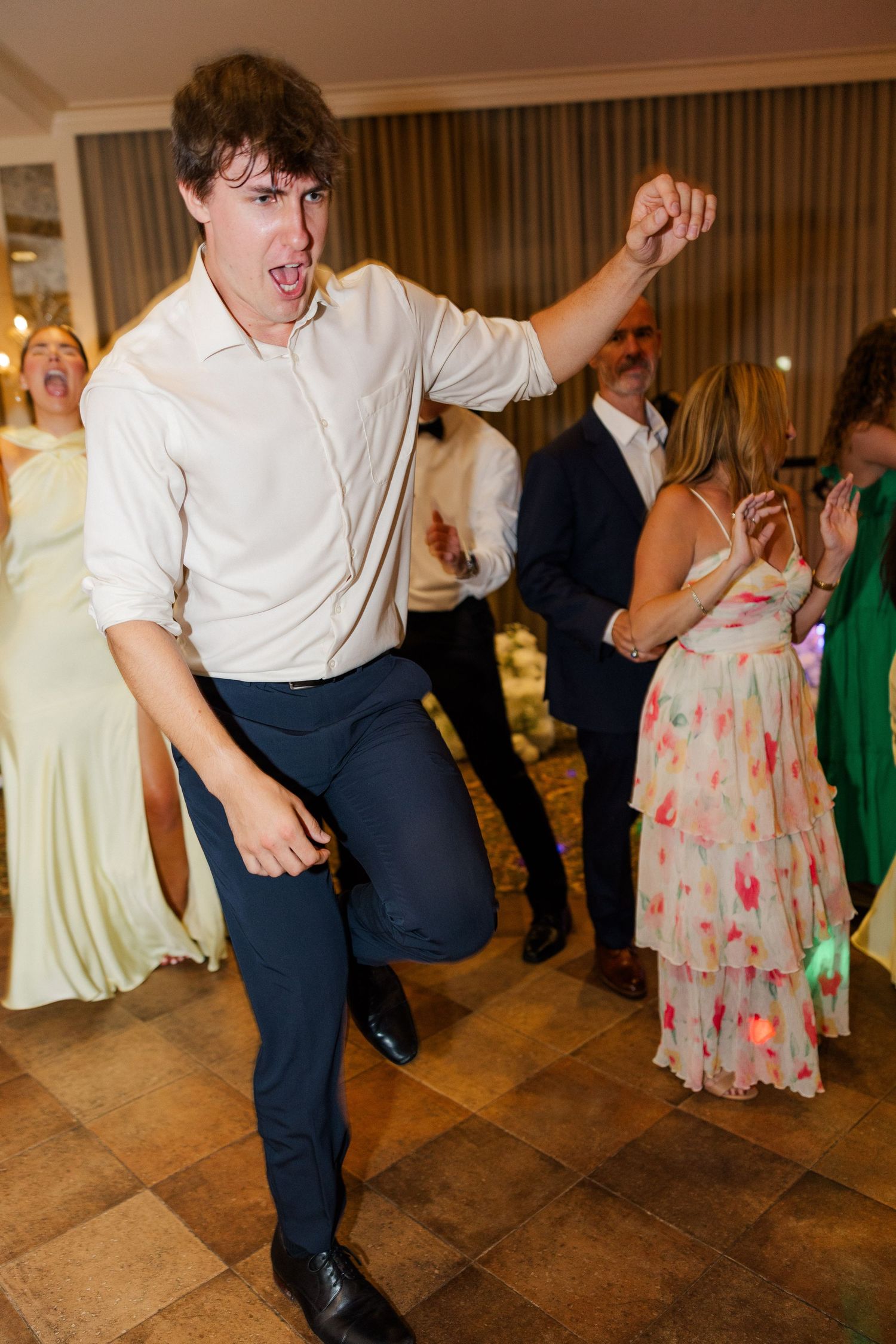 Wedding guest shows enthusiastic dance moves on wooden floor during reception.