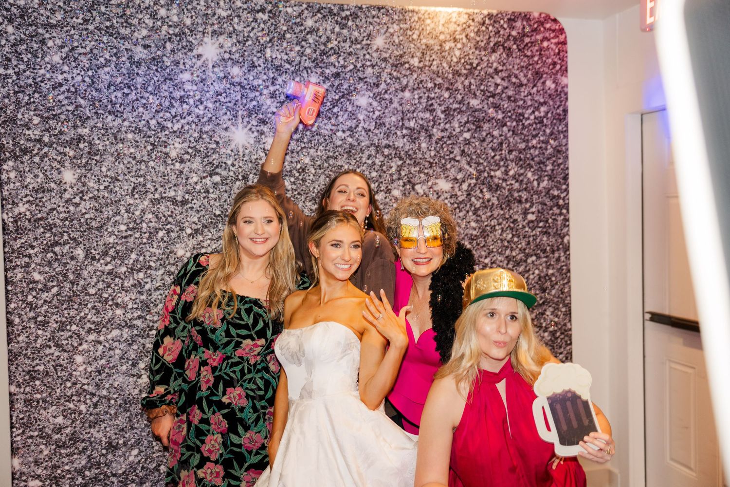 Wedding party poses in front of a sparkly backdrop with party props and confetti.