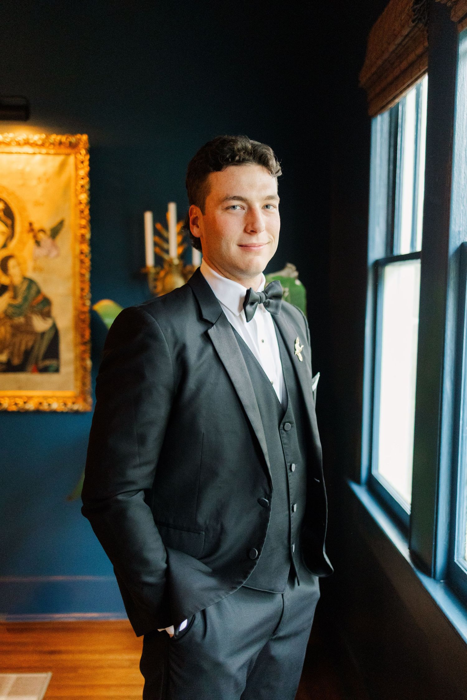 A formal portrait session near windows in a dark blue room with elegant gold-framed artwork on the walls.
