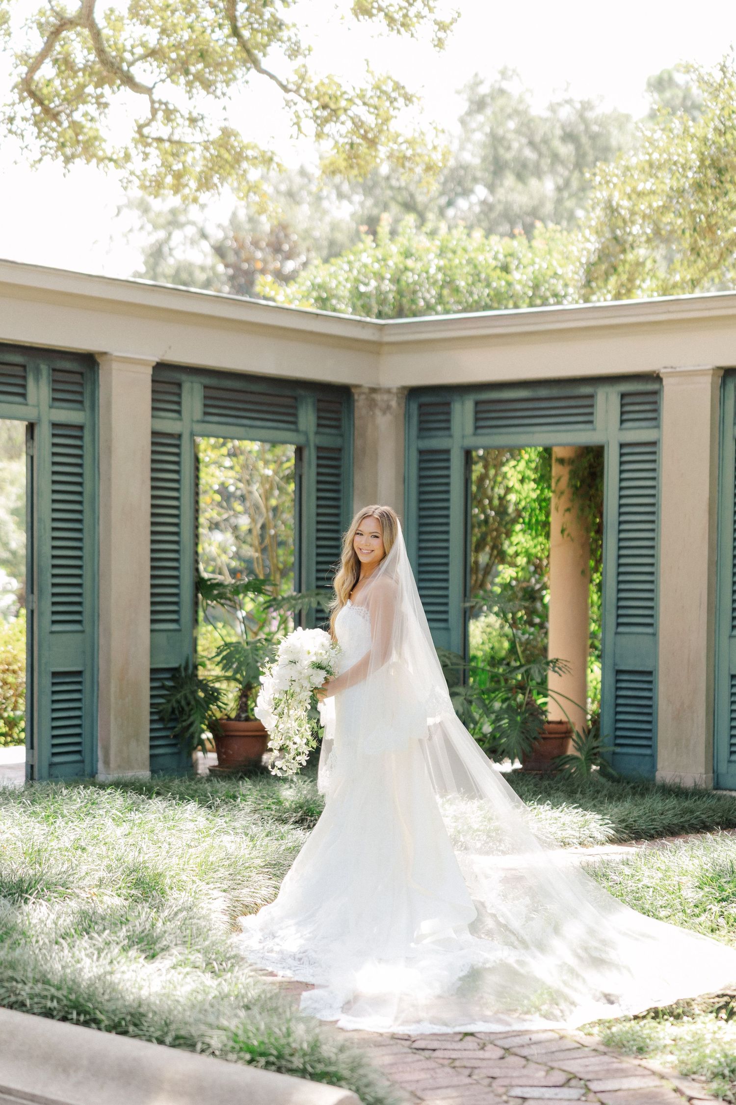 Elegant bridal portraits captured under a covered walkway with green shutters and natural lighting.