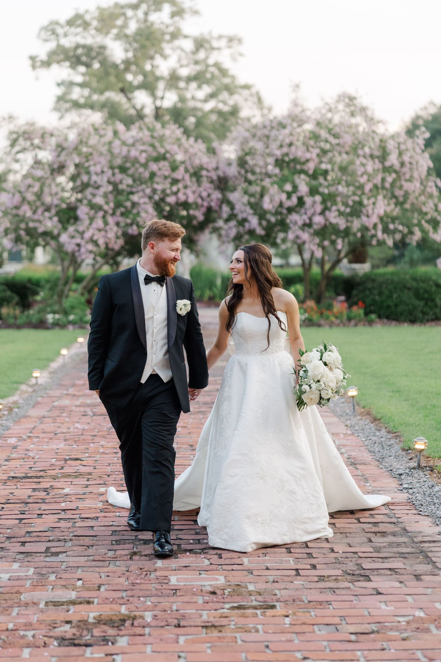 Newlyweds sharing romantic moment on brick pathway with spring blossoms in background.