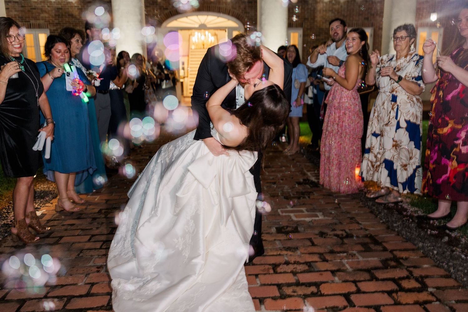 Wedding celebration on brick patio with guests dancing under string lights.
