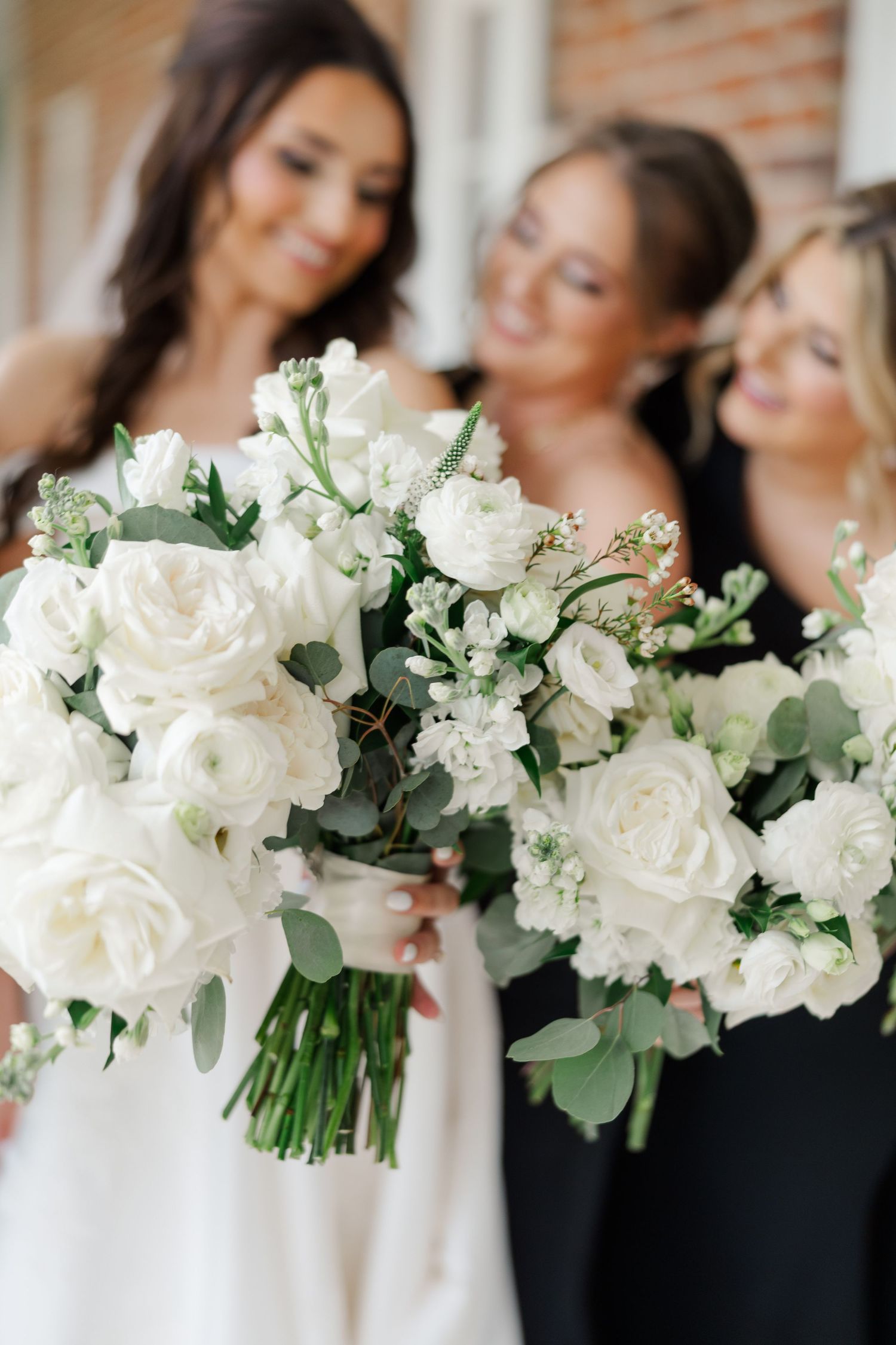 Row of elegant white rose and eucalyptus wedding bouquets arranged for bridal party photography.