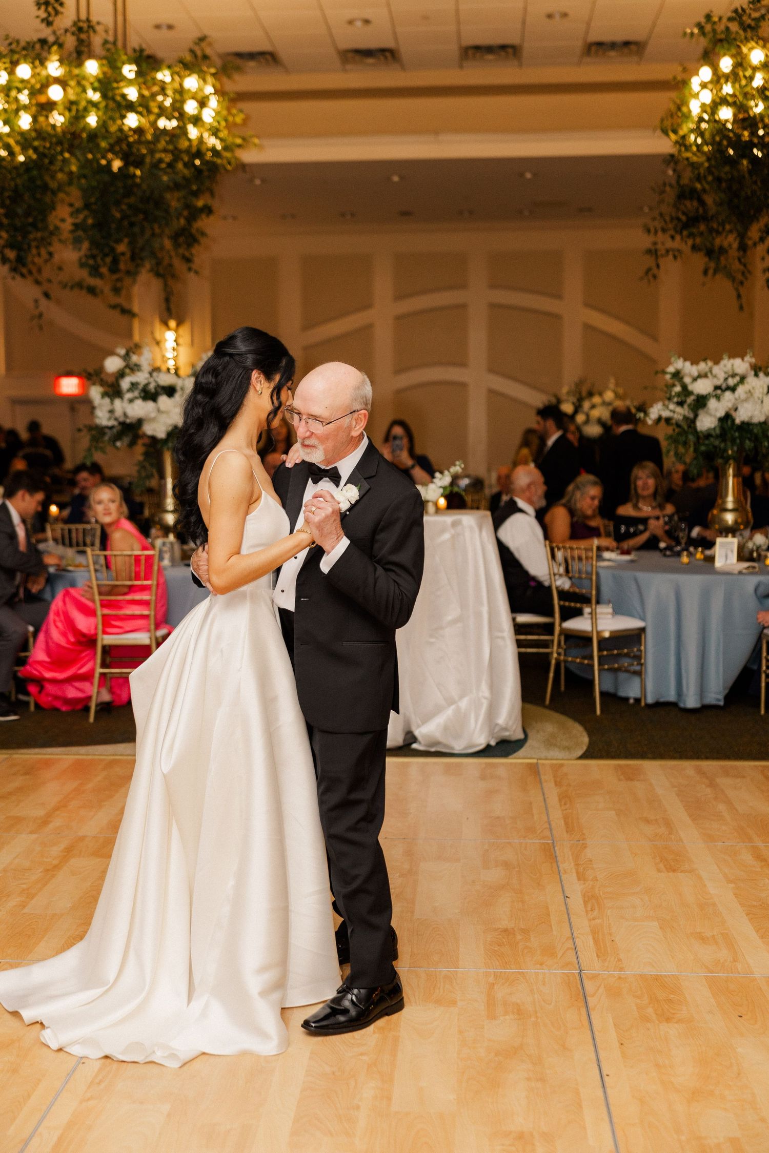 Bride and older gentleman sharing father-daughter dance in elegant ballroom reception venue.