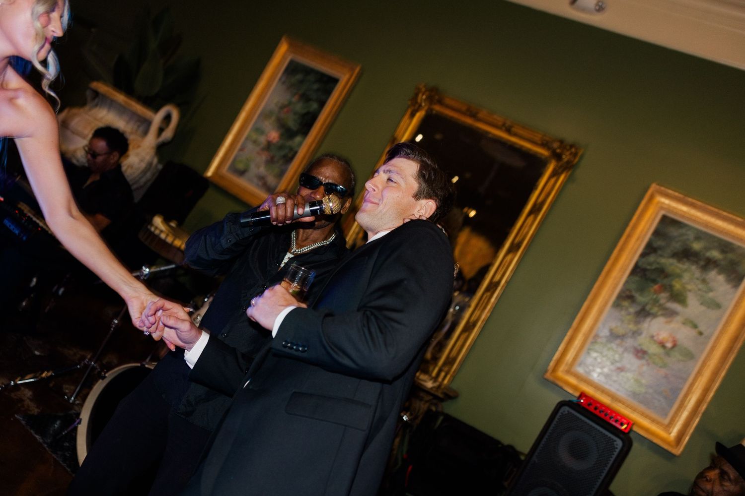 Singer performing energetically at elegant wedding reception in a dark suit, holding microphone on stage.