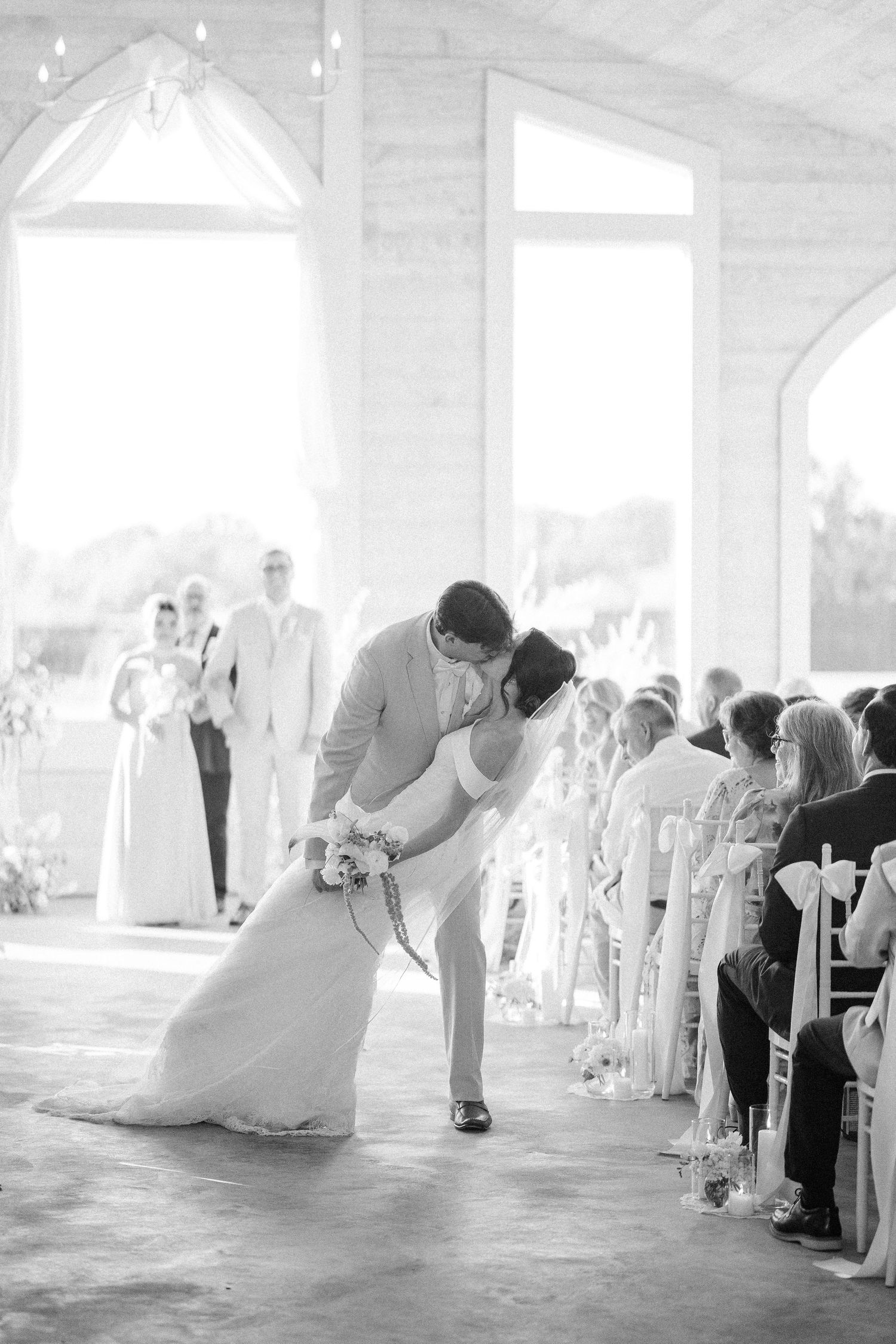 Black and white photo of groom dipping bride for a kiss in the aisle after their wedding ceremony.