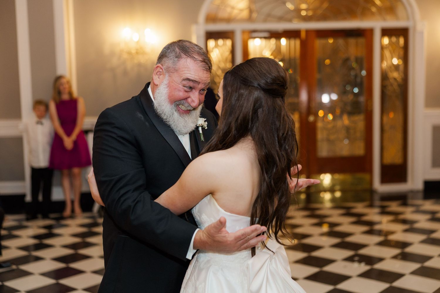An emotional father-daughter dance moment captured on a black and white checkered floor.