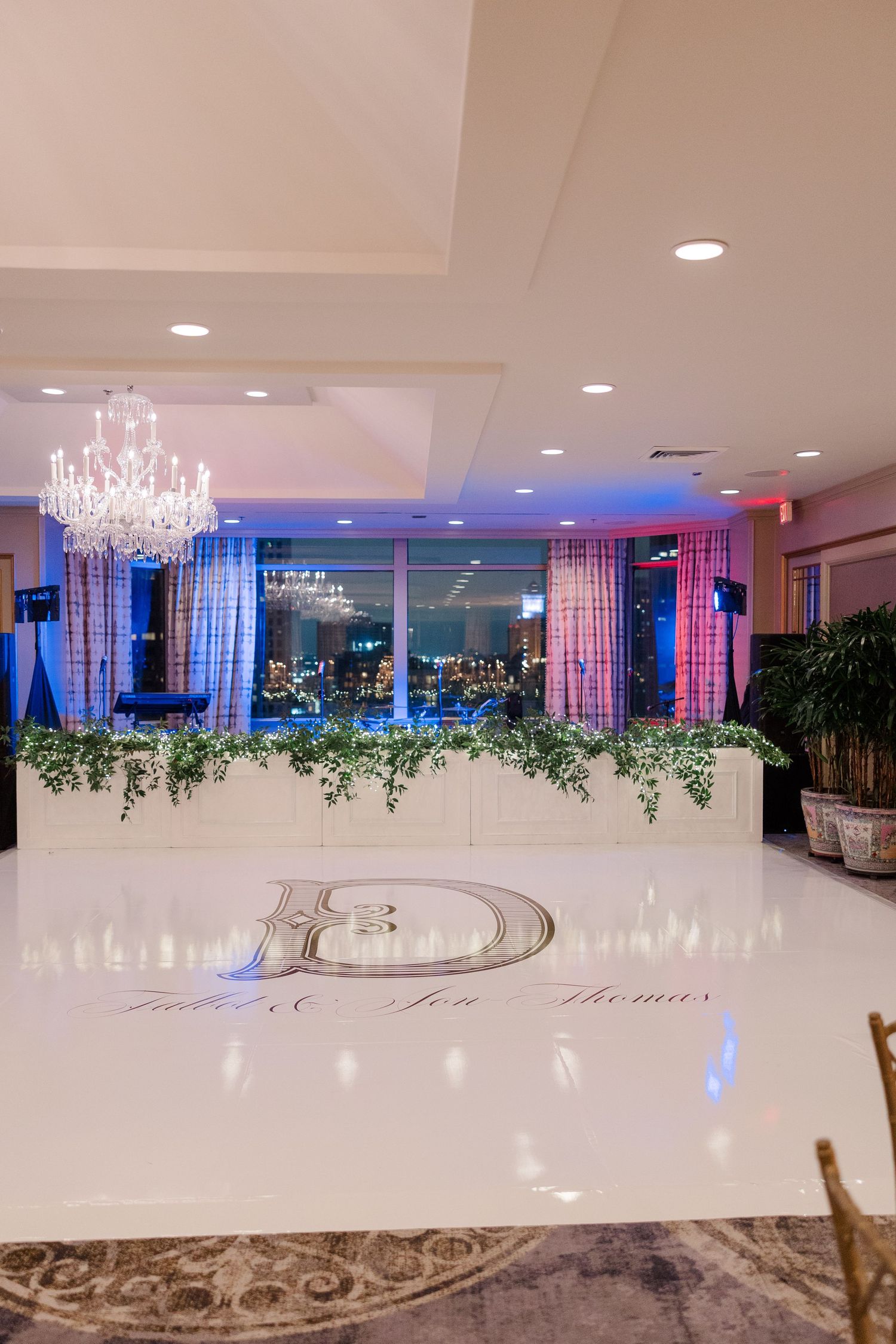 Modern event space with crystal chandeliers, colored lighting and city views through large windows.