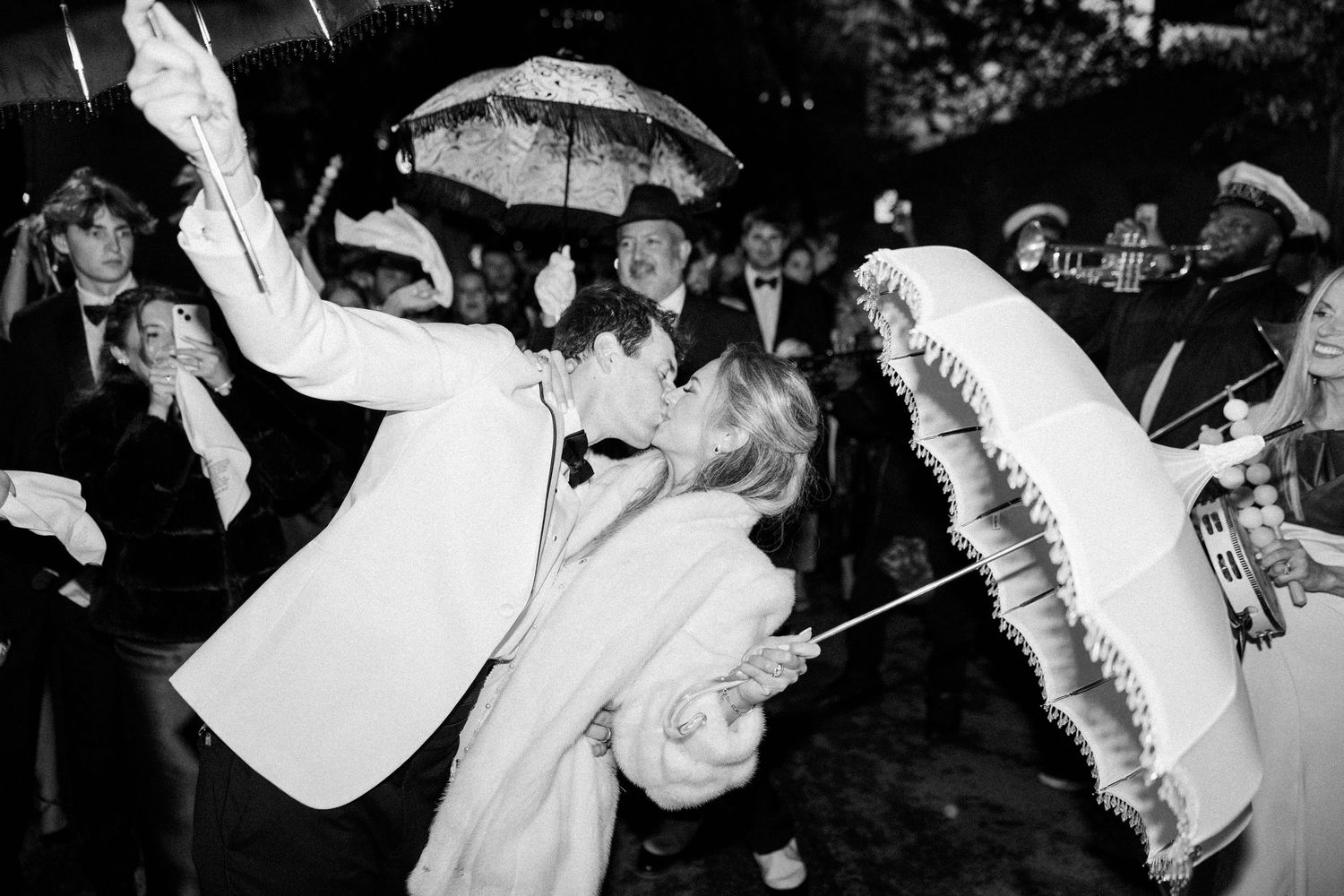 Black and white photo of wedding celebration with parasols and dancing in an energetic nighttime scene.