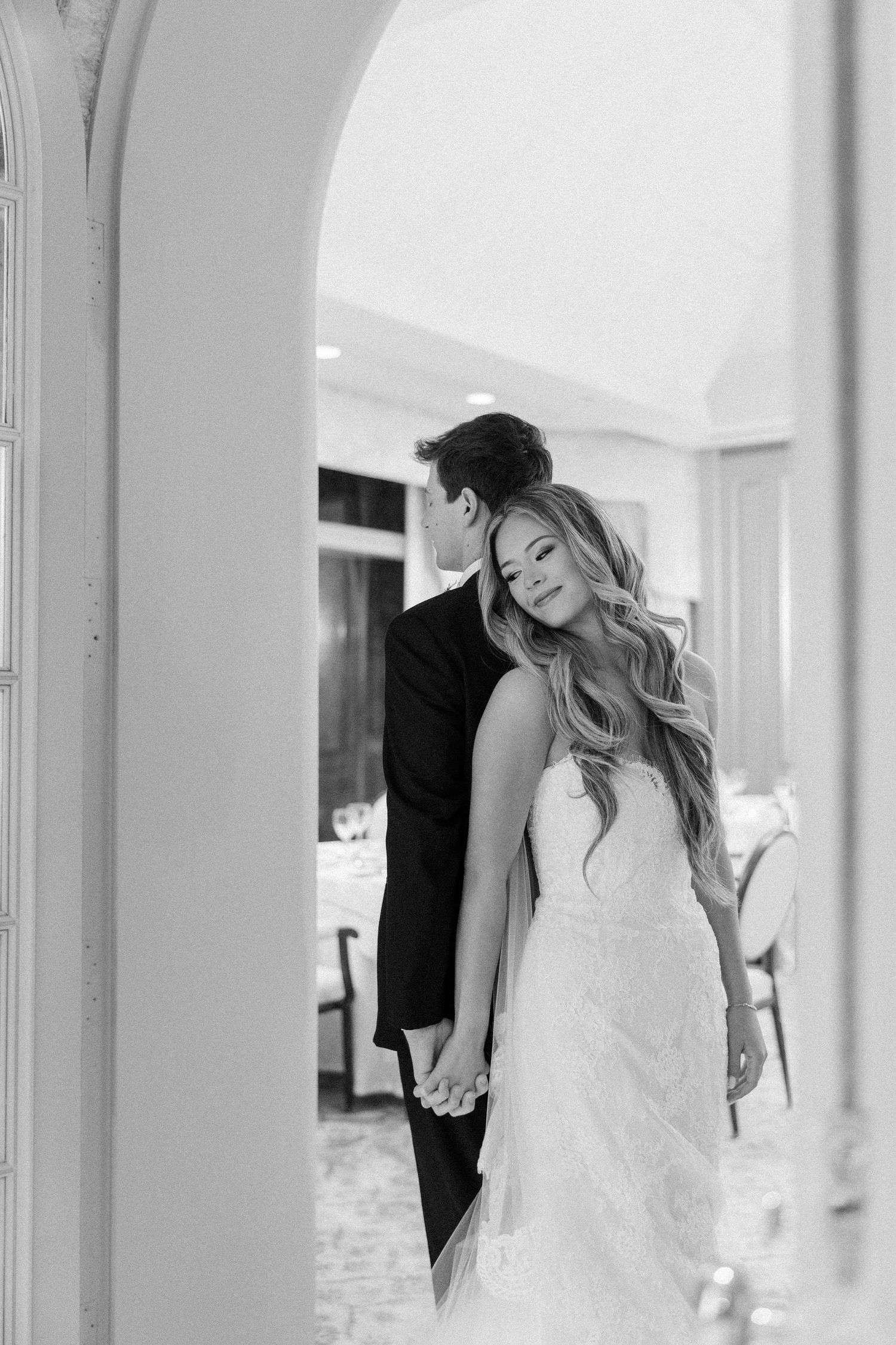 A romantic black and white wedding photo of a couple standing in an elegant archway.