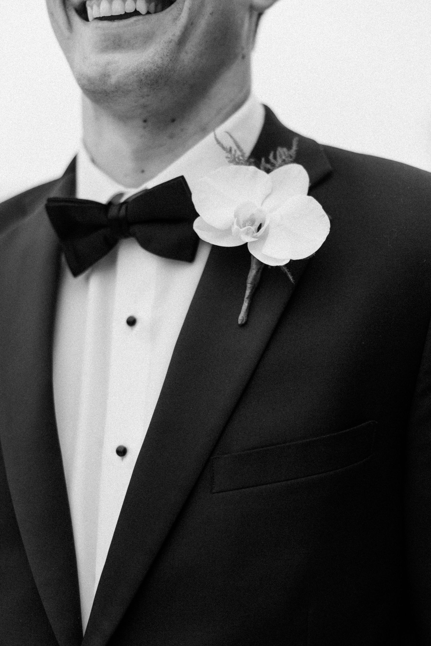 Close-up details of black tuxedo with white orchid boutonniere and bow tie.