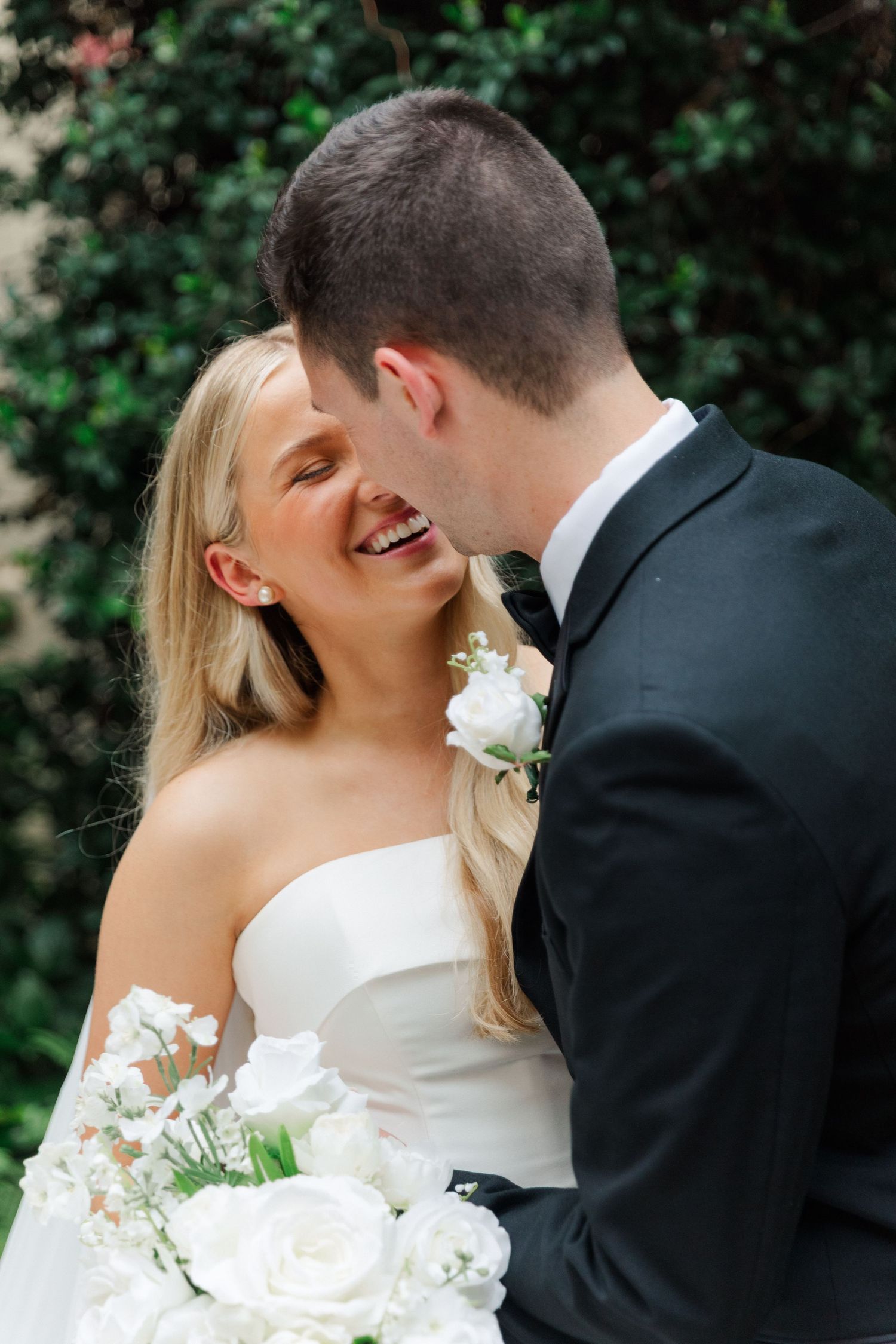 Intimate wedding moment captured in a garden setting with white floral bouquet.