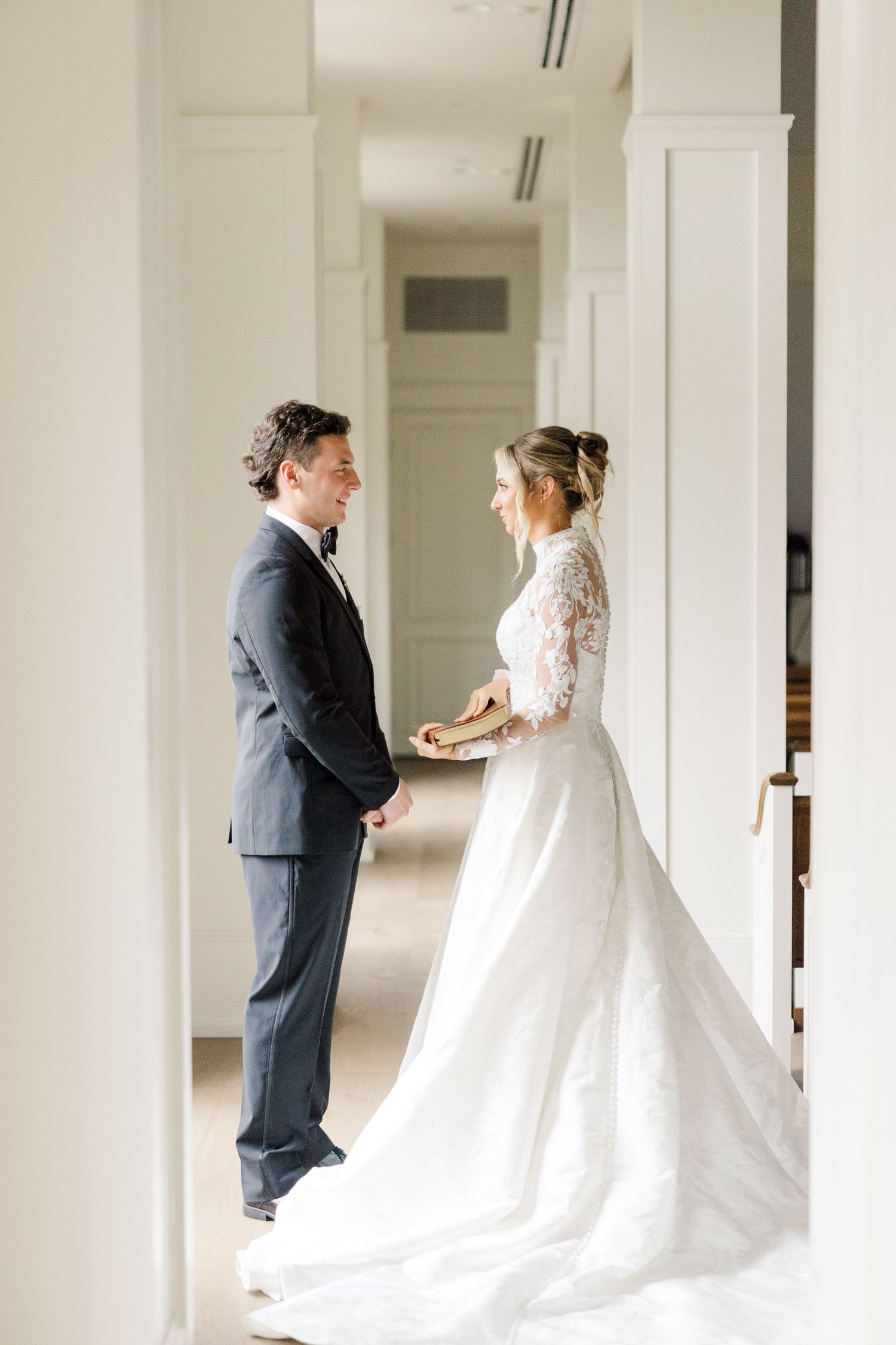 First look moment between bride and groom in white hallway with columns.