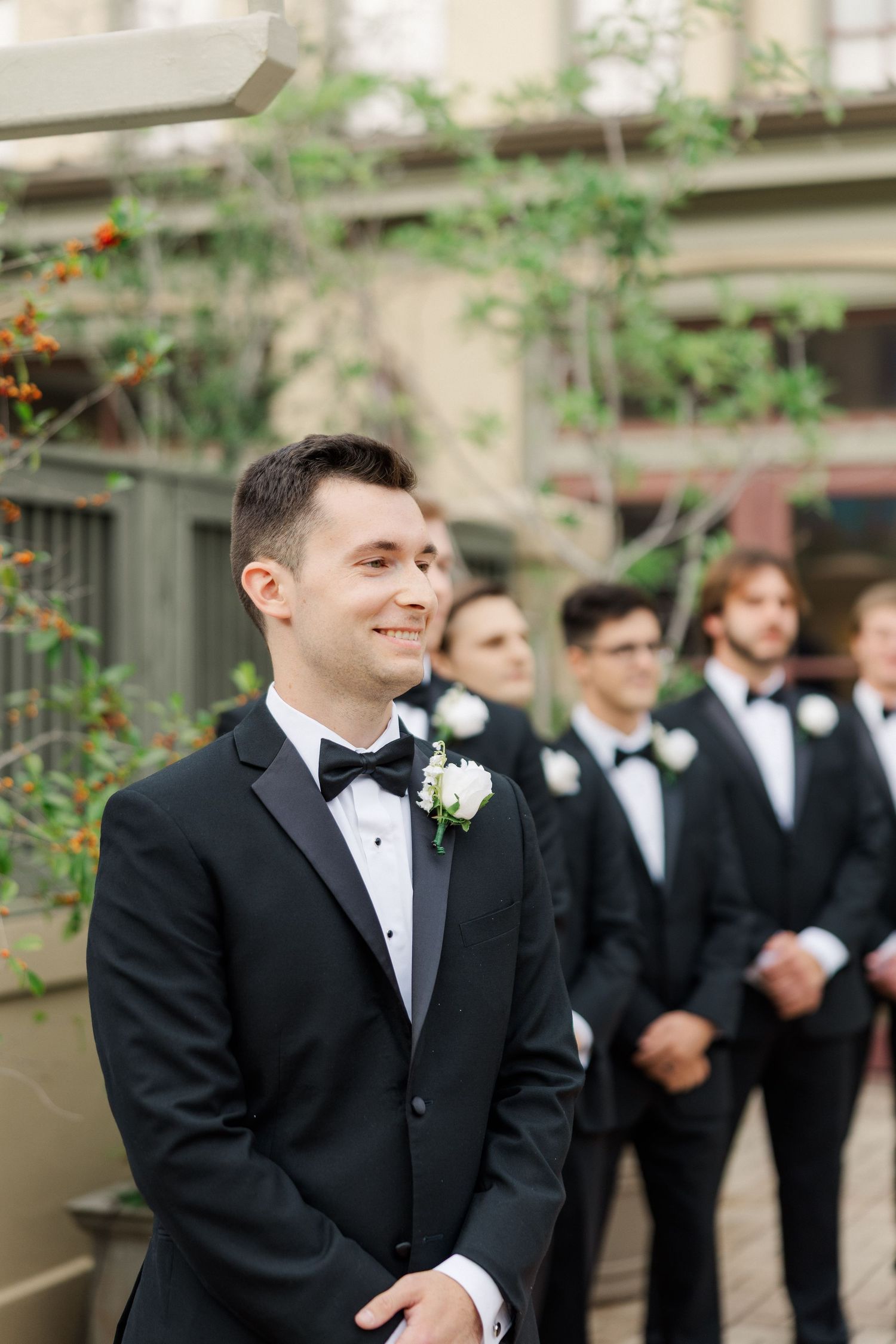 Groomsmen in classic black tuxedos gather outdoors for formal wedding photos.