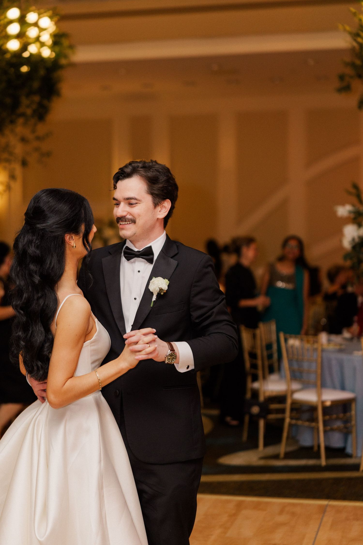 Bride and groom share their first dance in a warmly lit elegant ballroom reception venue.