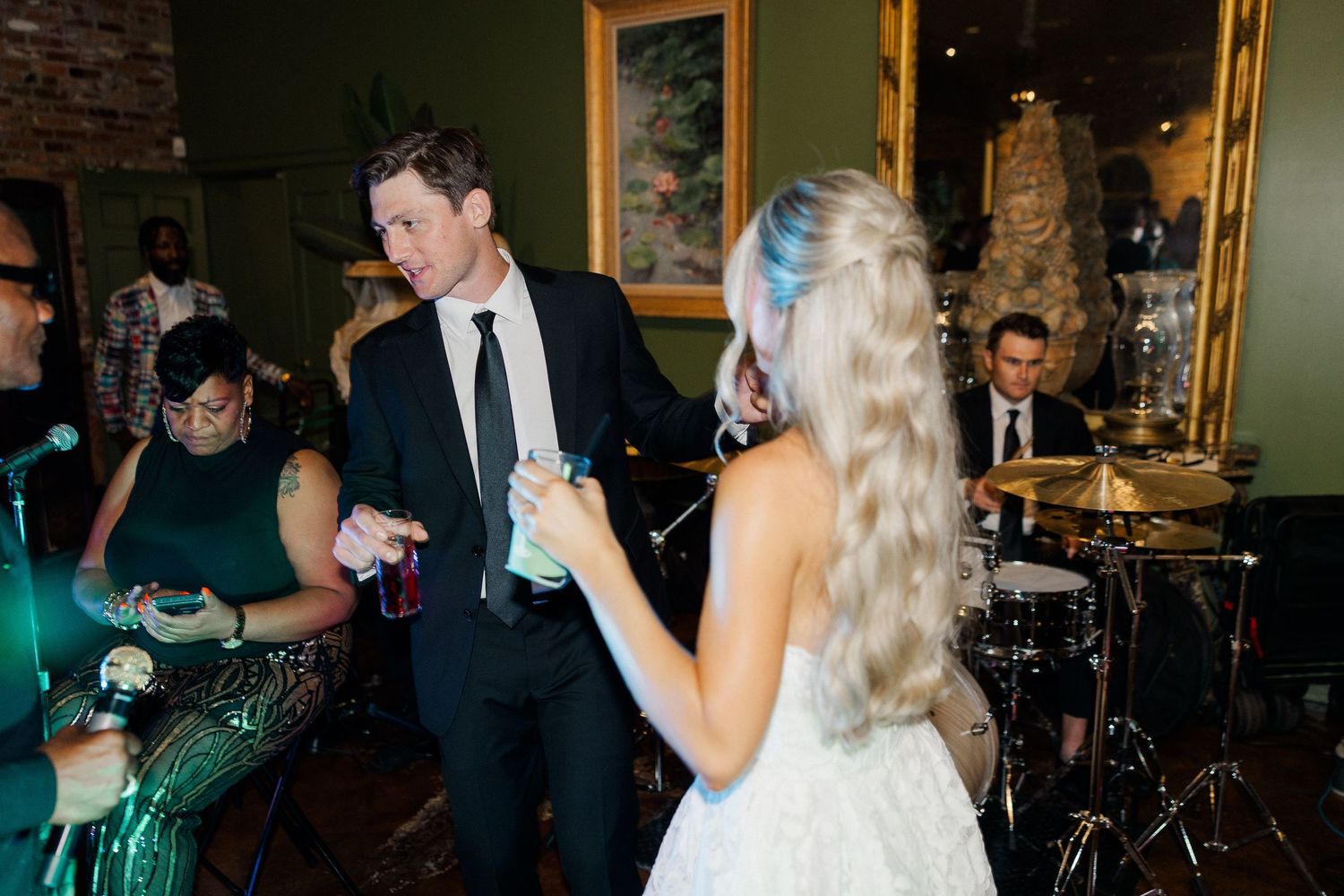 Bride in white dress dances with groom in black suit at lively indoor wedding reception with live band.