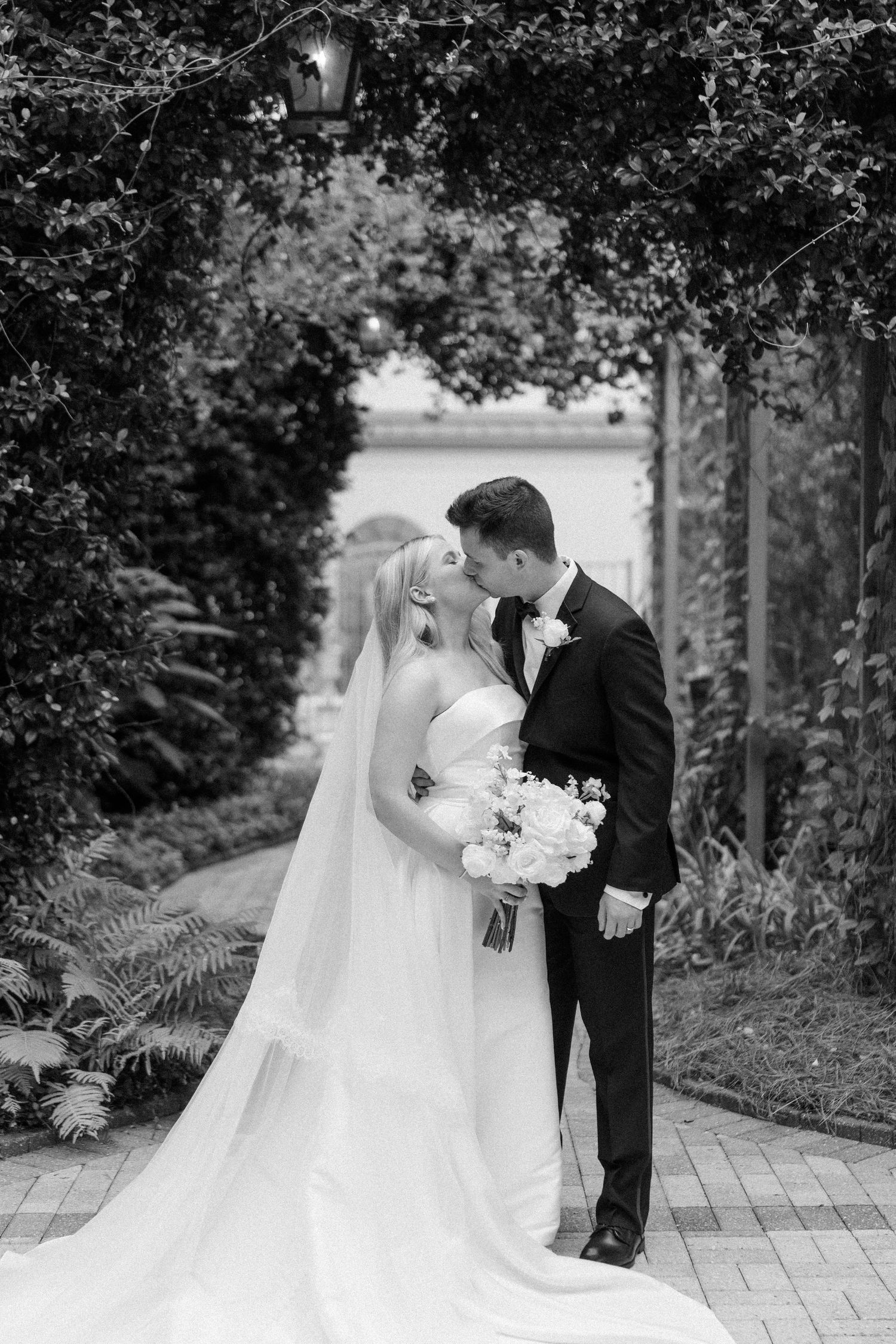 Black and white wedding portraits of couple on a garden pathway with flowing veil.