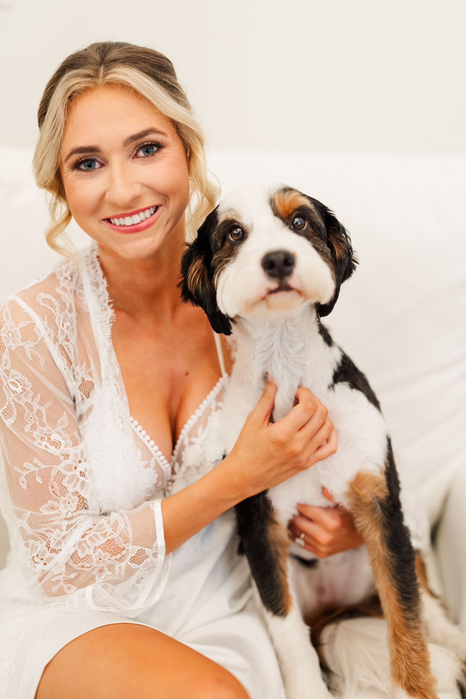 A black and white dog sits with someone wearing a white lace robe in a bright indoor setting.