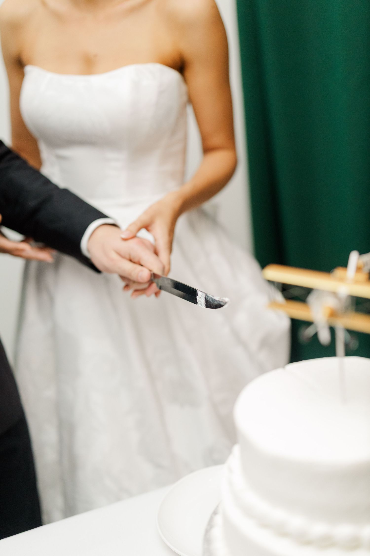 Close-up of hands cutting into a classic white wedding cake.