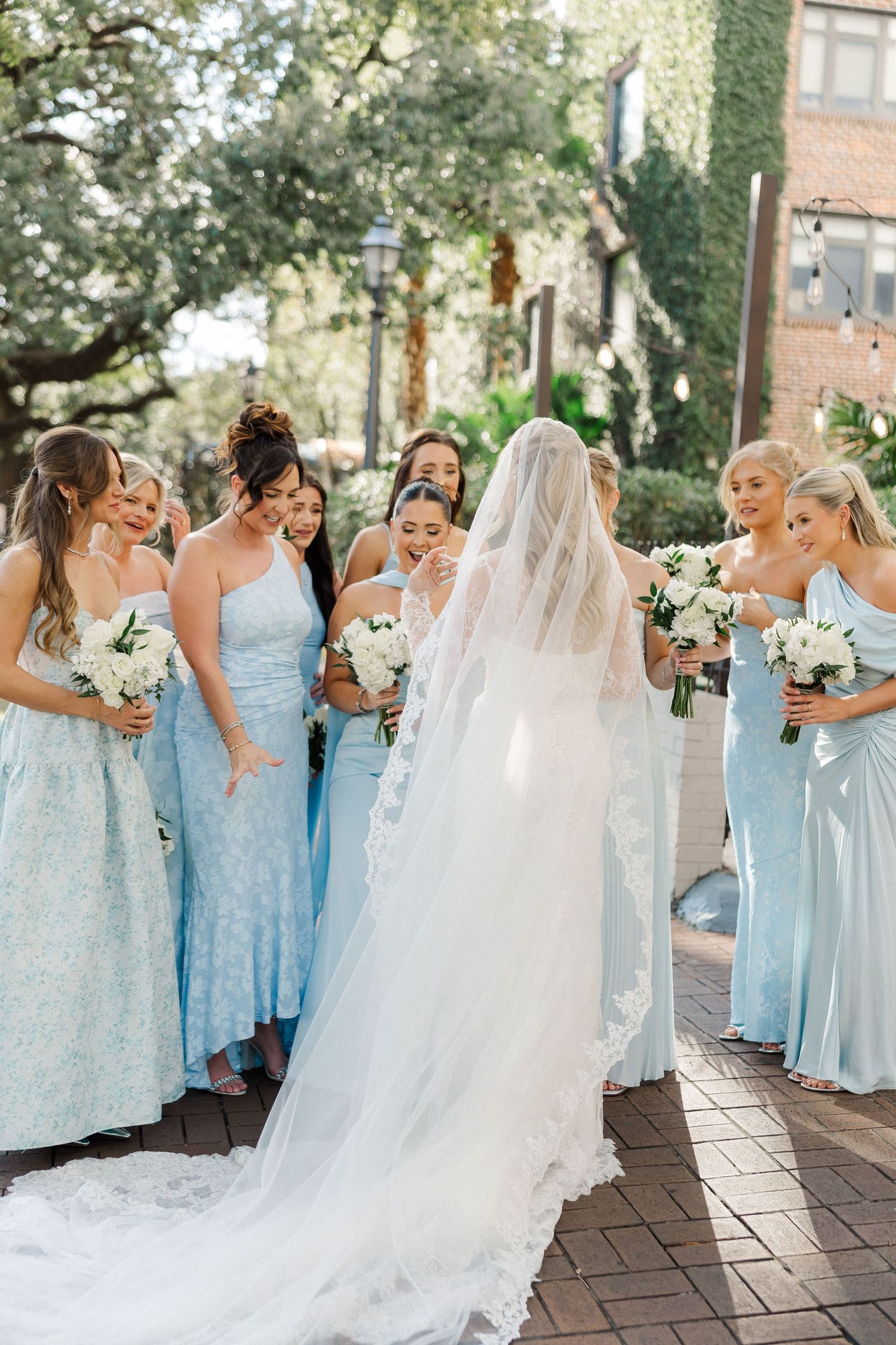 Wedding party in light blue bridesmaid dresses walking together on brick pavement.