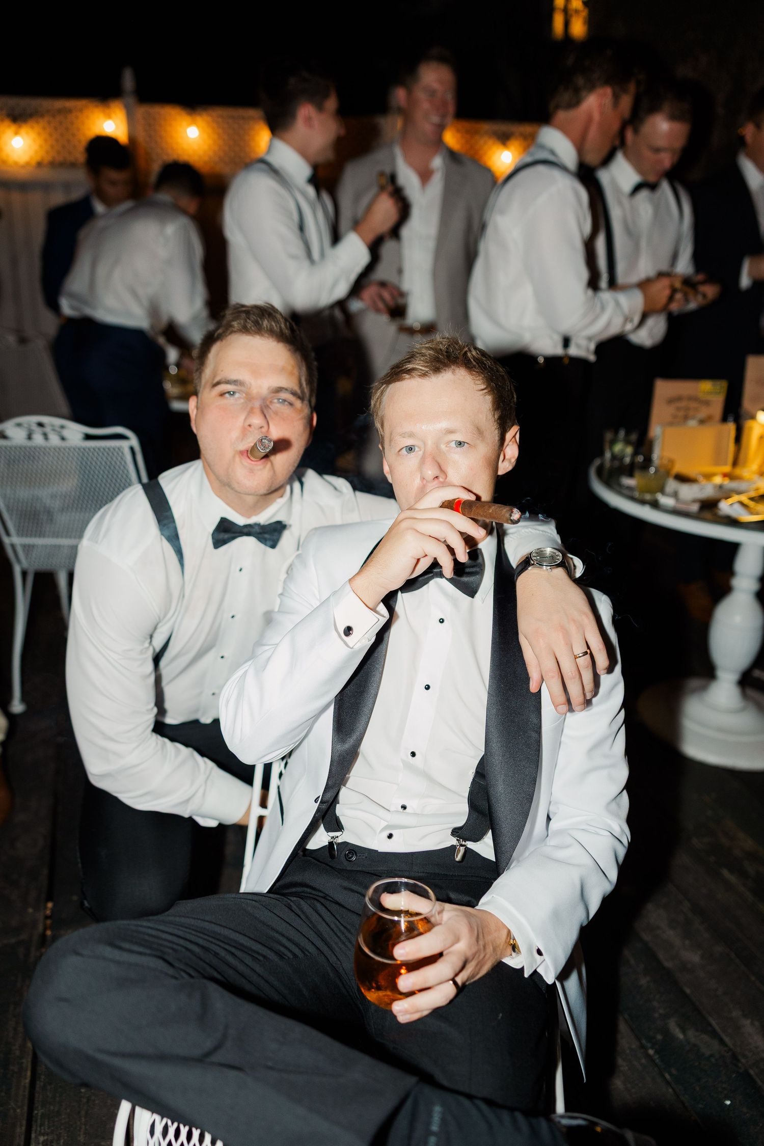 Groomsmen in tuxedos and bowties enjoying drinks at the wedding reception.