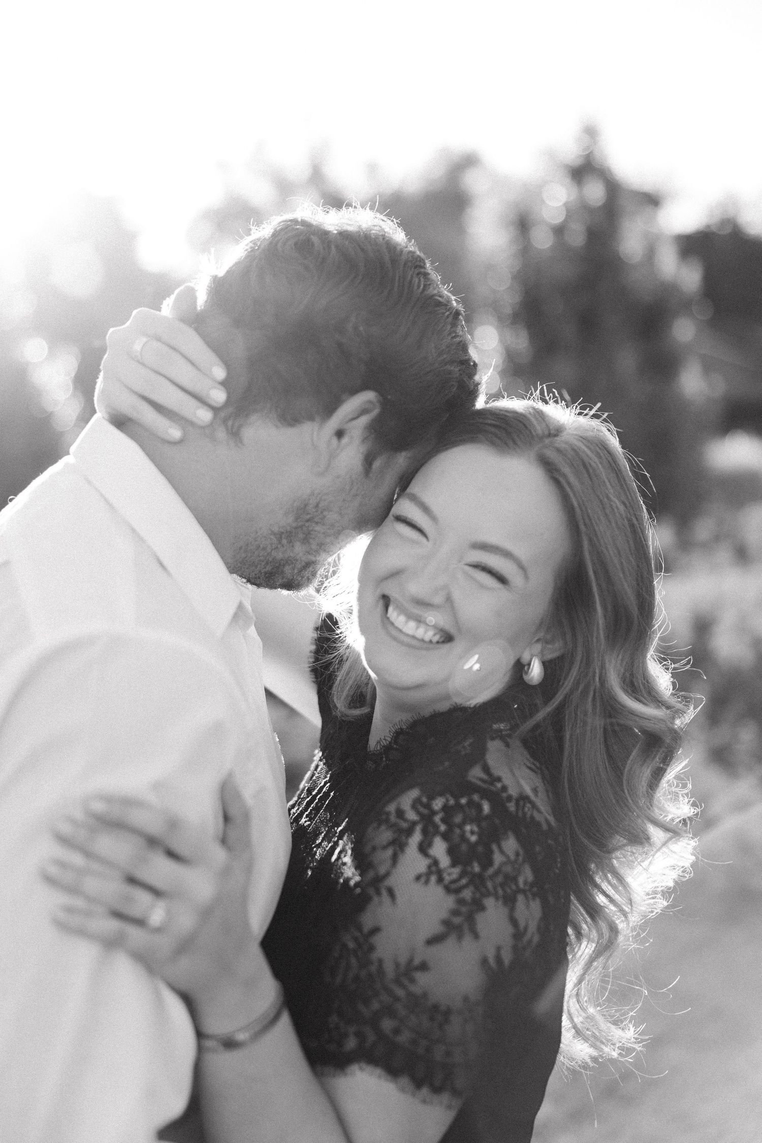 A romantic black and white photo series showing a couple embracing and laughing together outdoors in natural light.