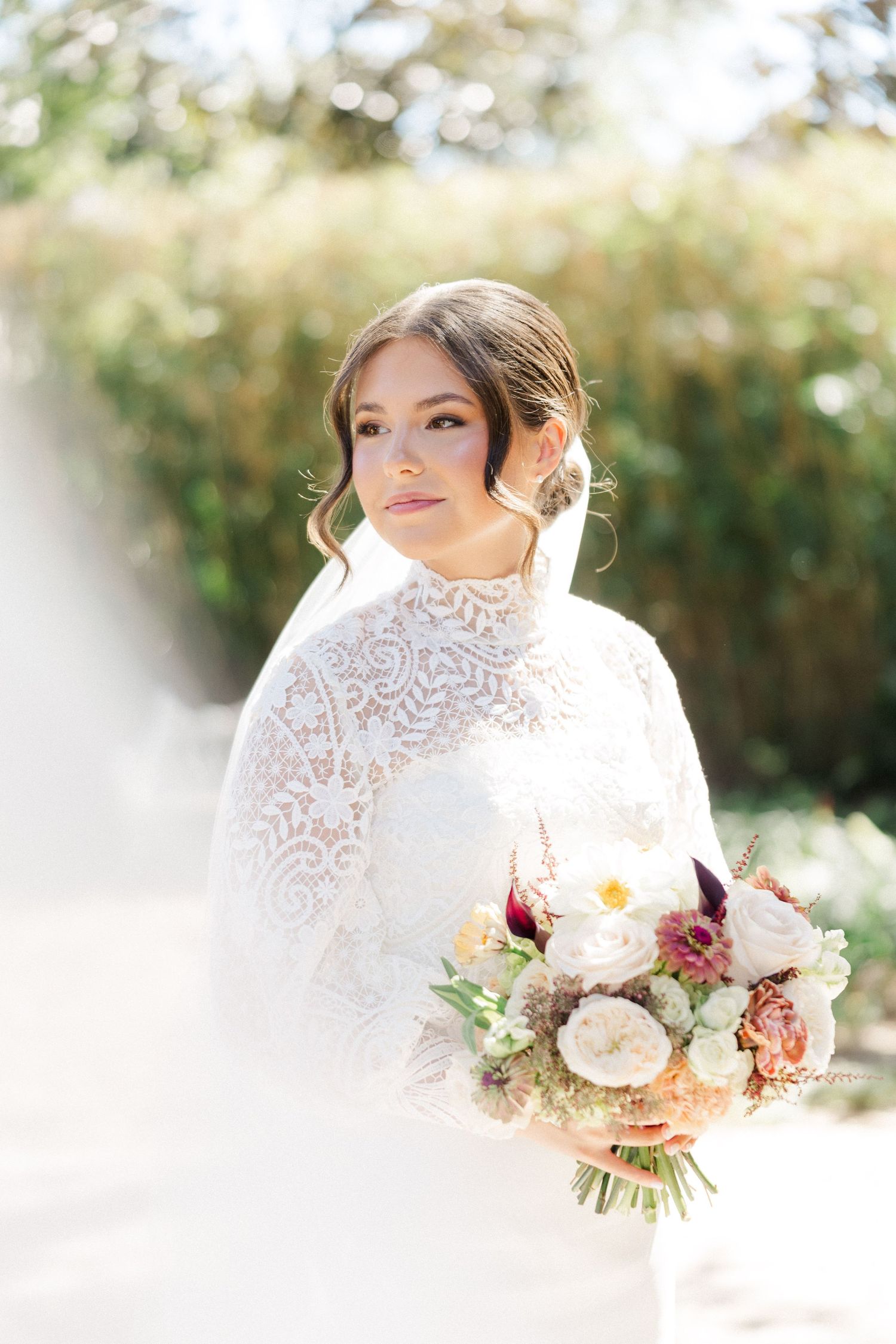A dreamy bridal portrait showcasing an elegant lace wedding gown and romantic bouquet in soft natural light.