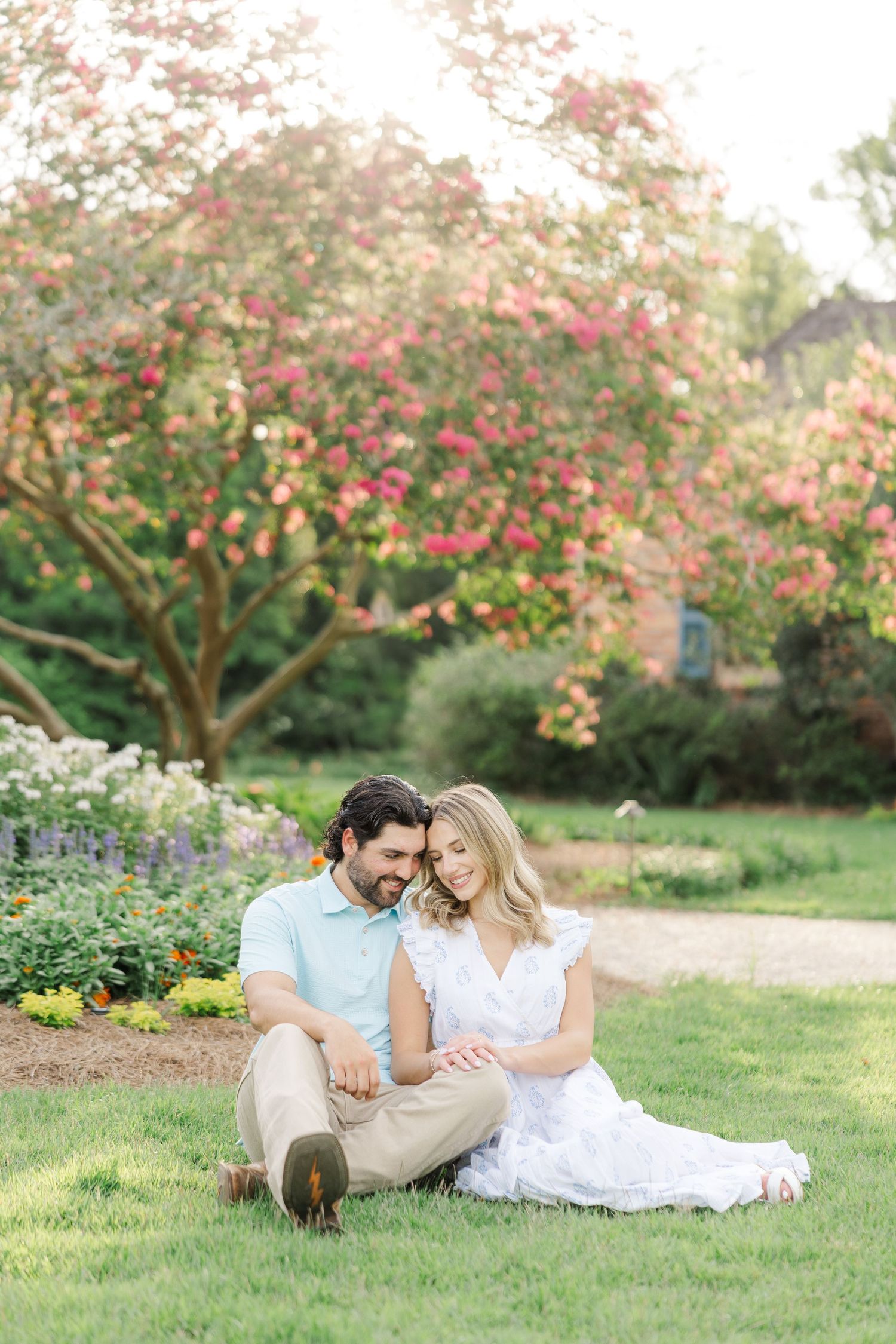 A couple relaxes and shares intimate moments while laying on grass under flowering trees in a garden.