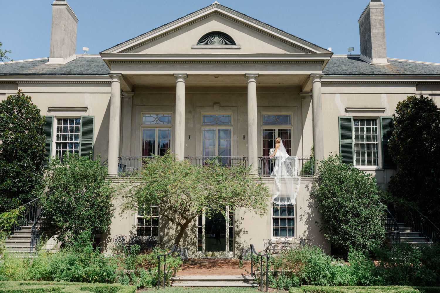 Historic mansion with neoclassical columns and symmetrical design features manicured landscaping and dual chimneys.