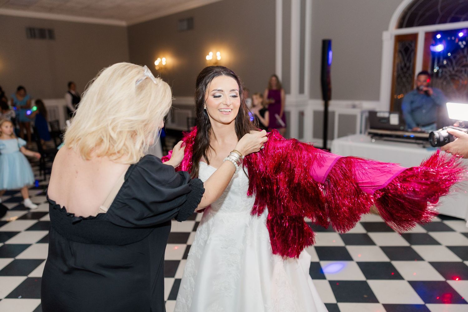 A bride in a white gown dances with a red feather boa on a black and white checkered floor.