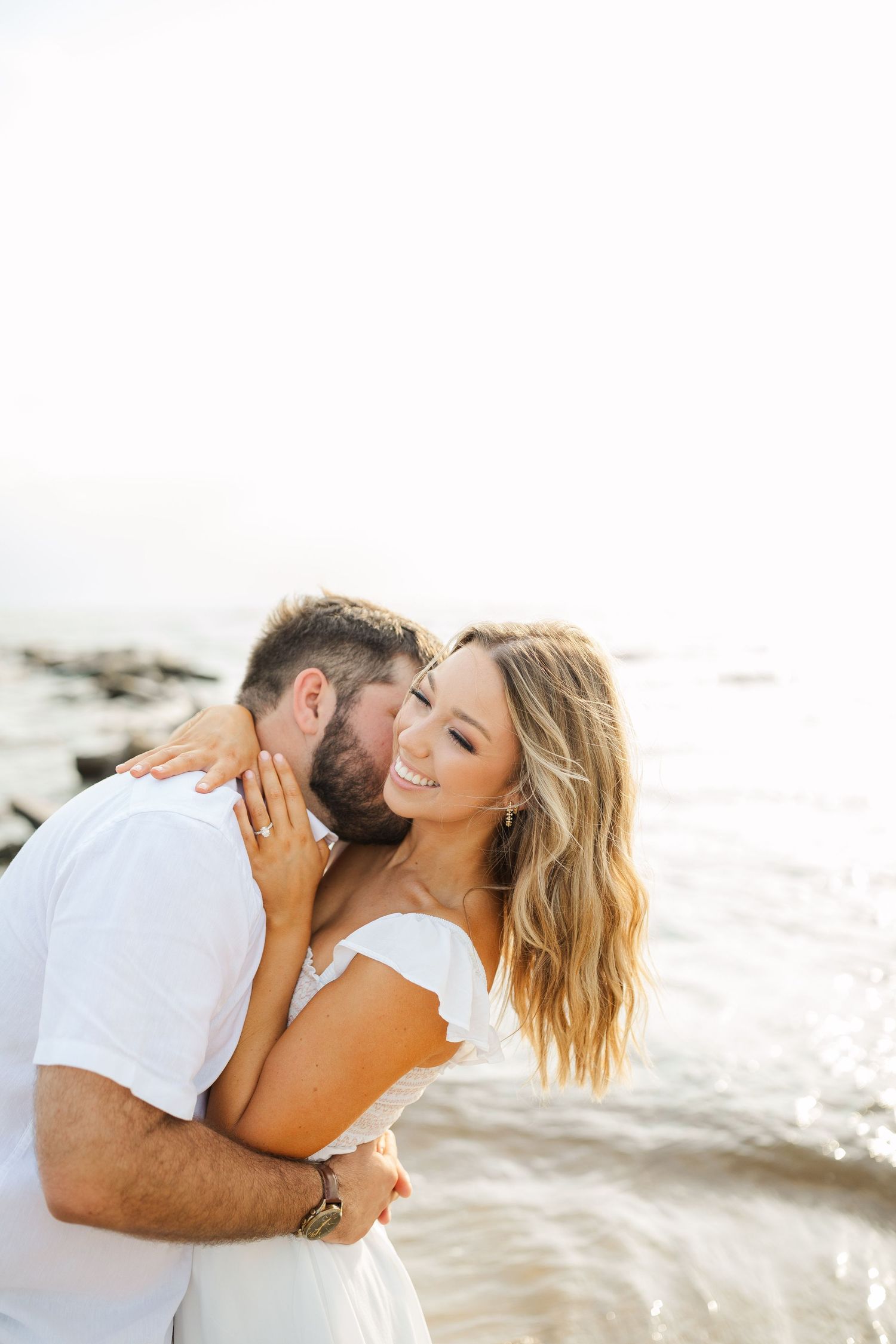 A loving couple shares an intimate moment on the beach during sunset in white summer outfits.