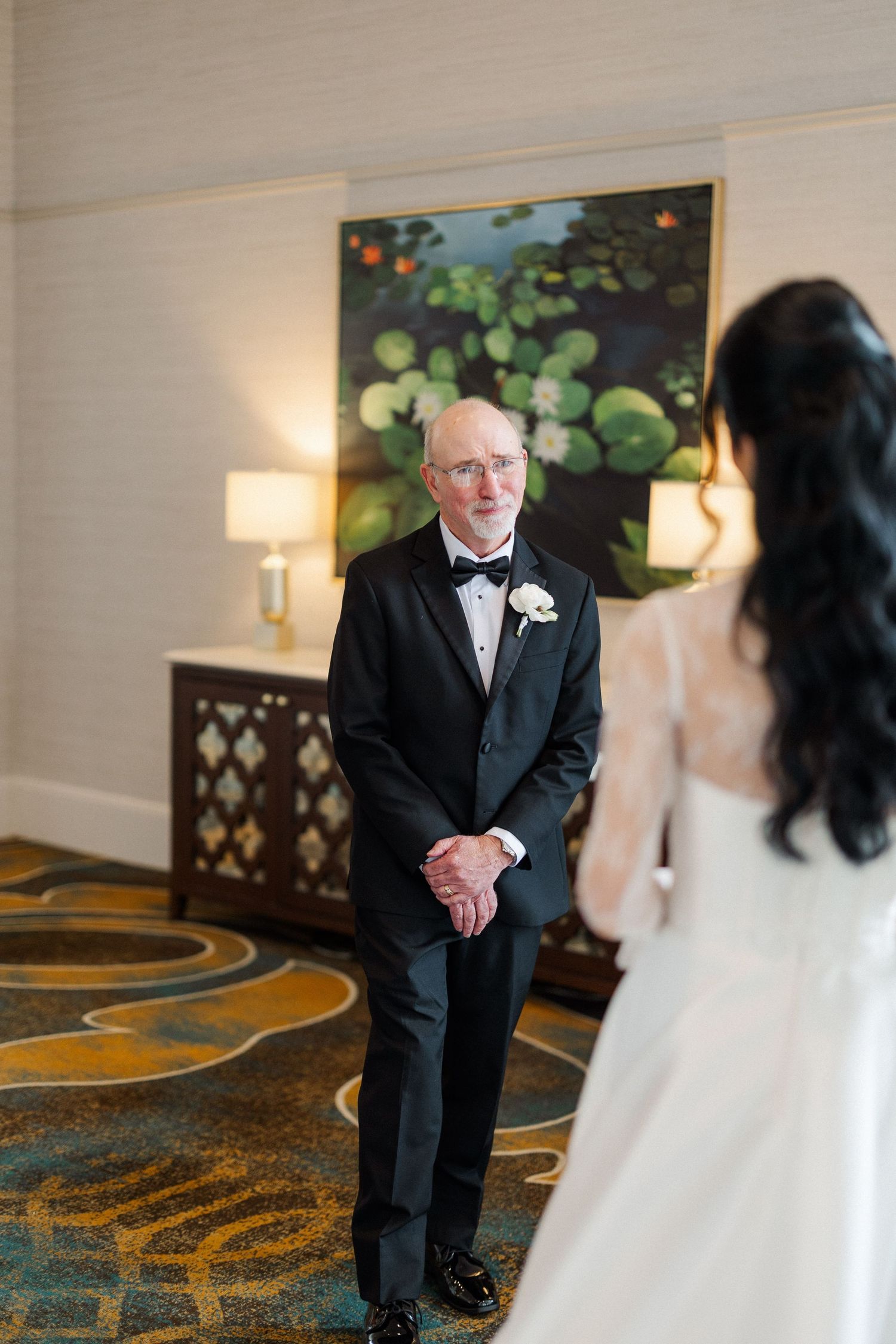 Father seeing bride in wedding dress for the first time, emotional first look moment in elegant hotel.