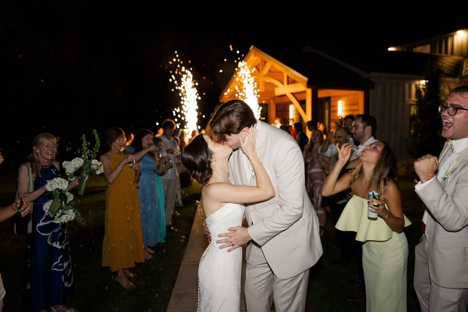 Newlyweds share a romantic kiss during their sparkler send-off exit at their outdoor evening wedding reception.