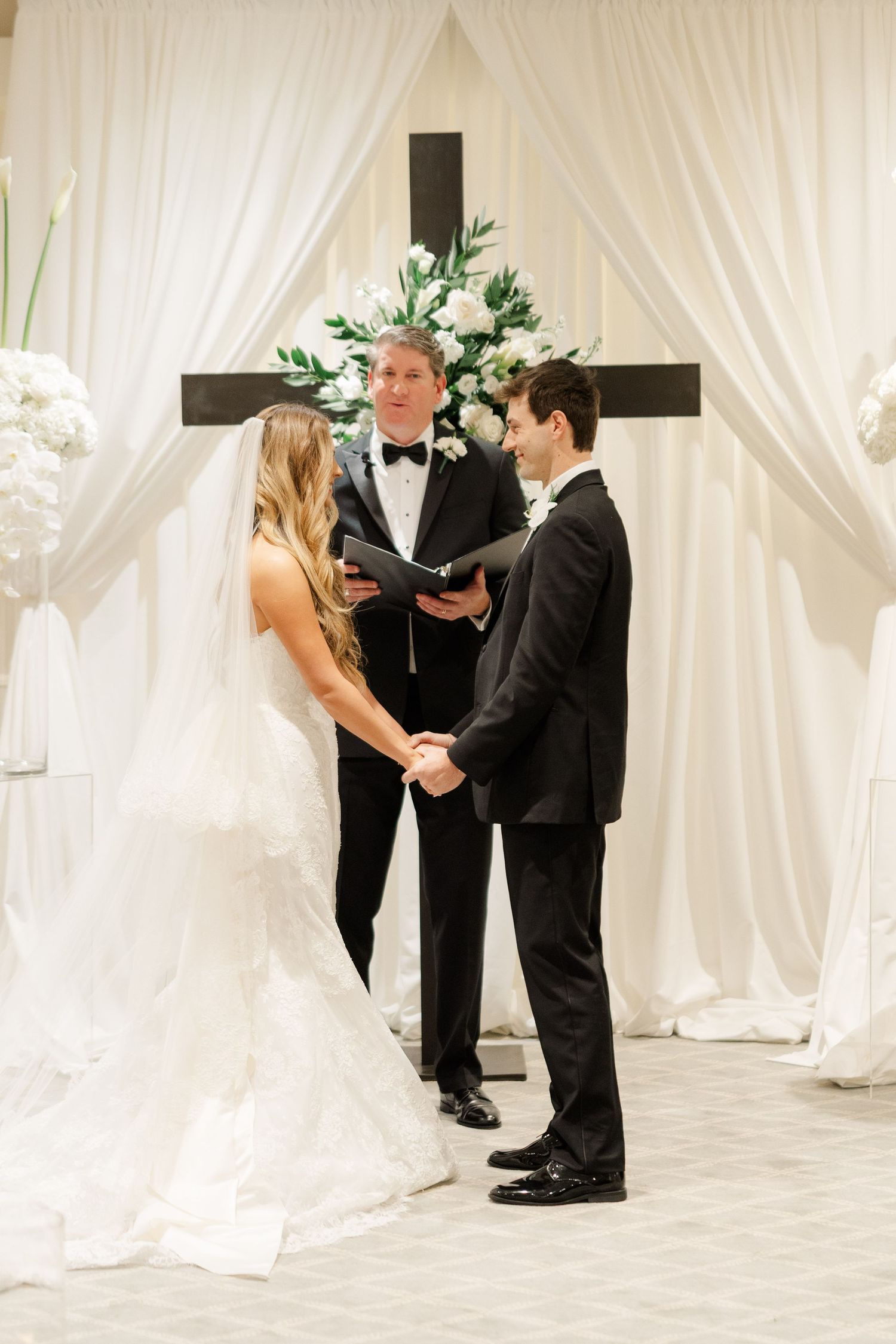 A wedding ceremony under a white draped altar with cross and floral arrangements.
