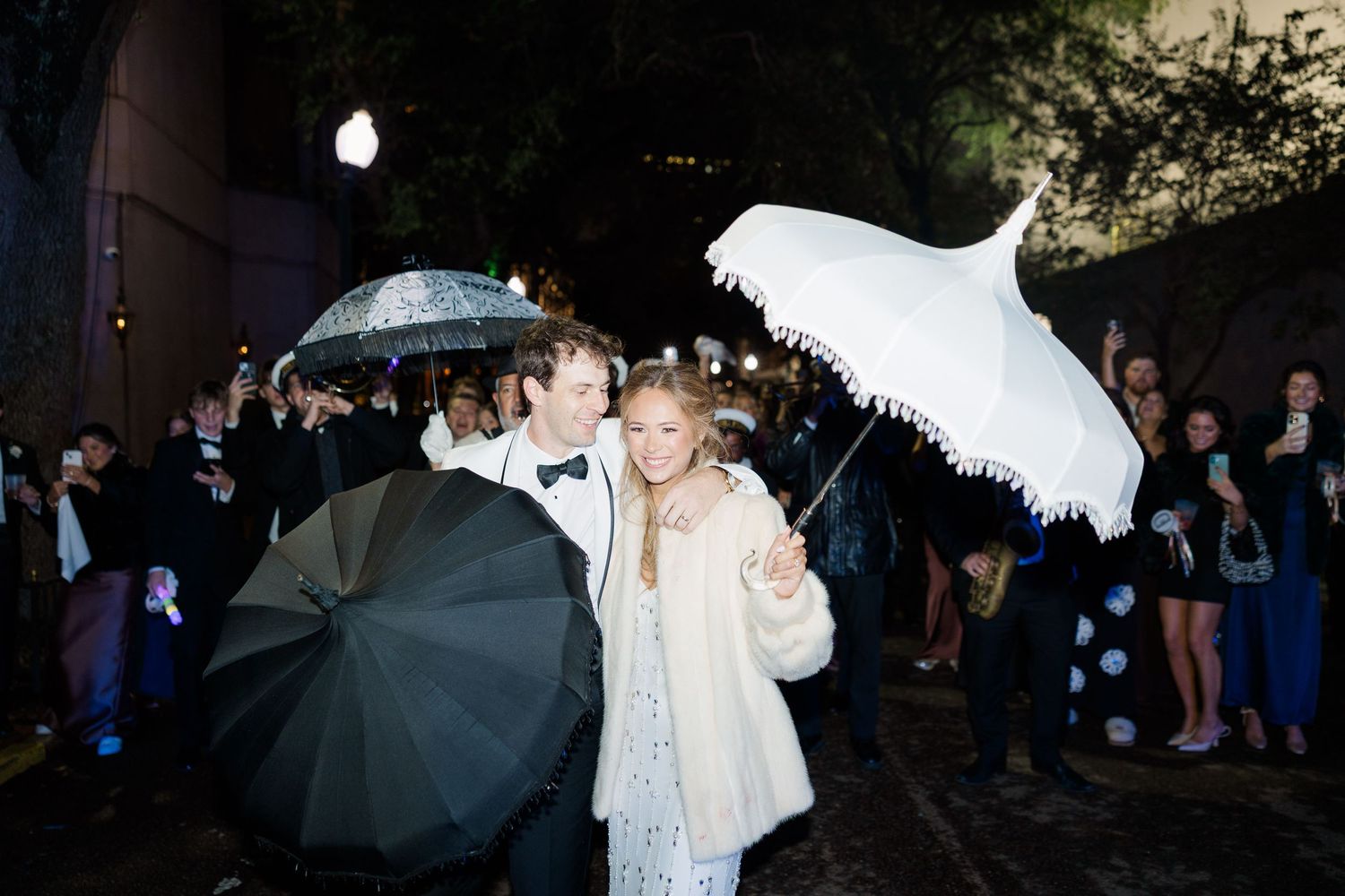 Wedding guests with umbrellas celebrate during an outdoor nighttime celebration.