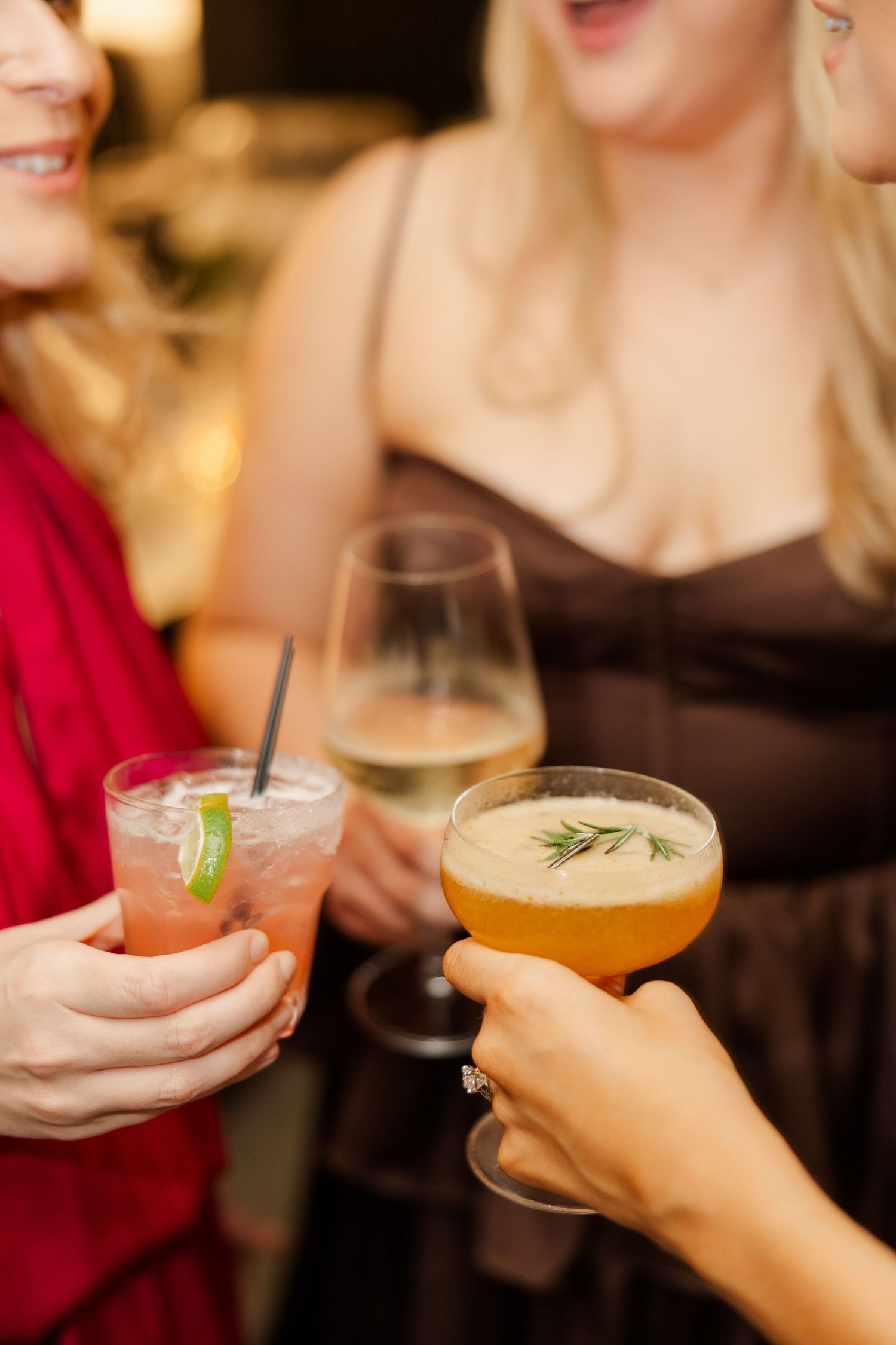 Guests hold colorful craft cocktails garnished with herbs during wedding reception.