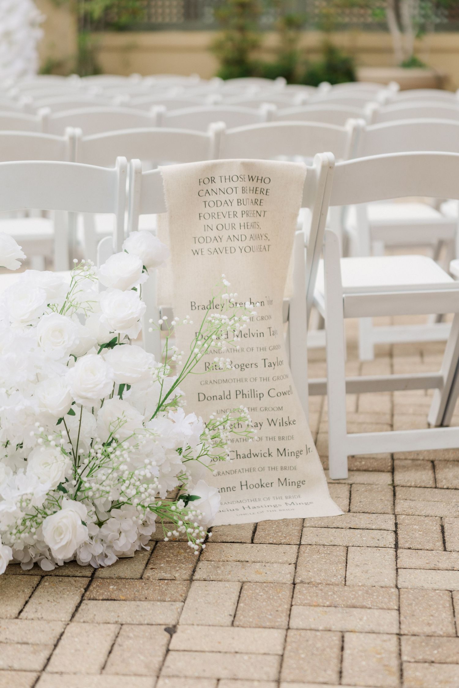 White floral arrangements decorating ceremony chairs with printed name cards on stone pavers.