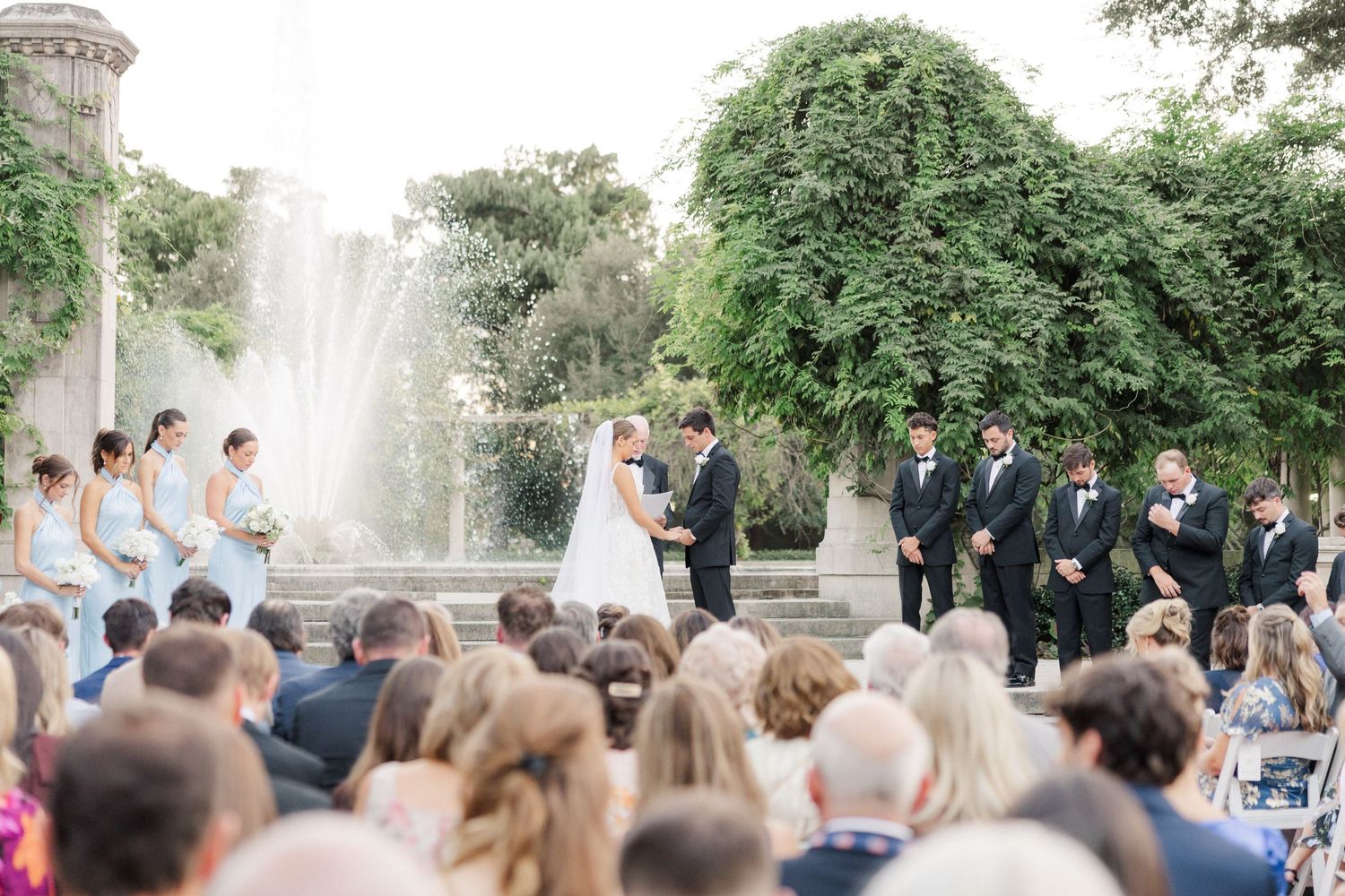 A wide view of an outdoor wedding ceremony with guests seated beneath trees.
