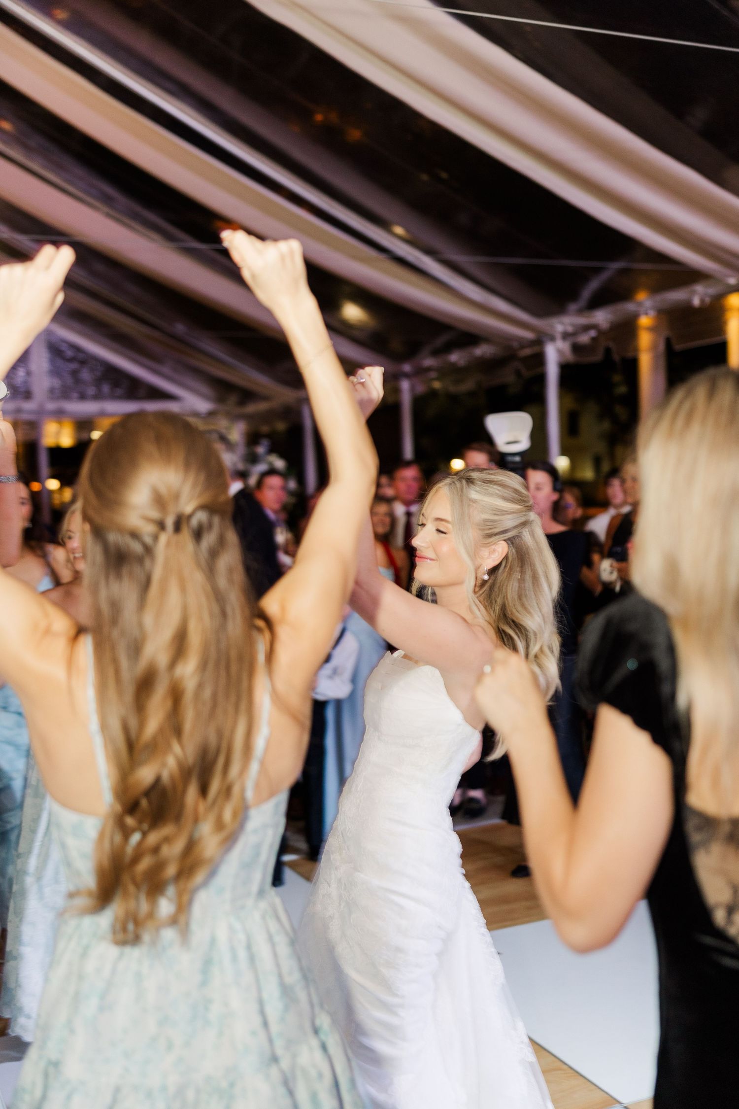 Wedding celebration with guests dancing and raising their hands in joy under a tent.