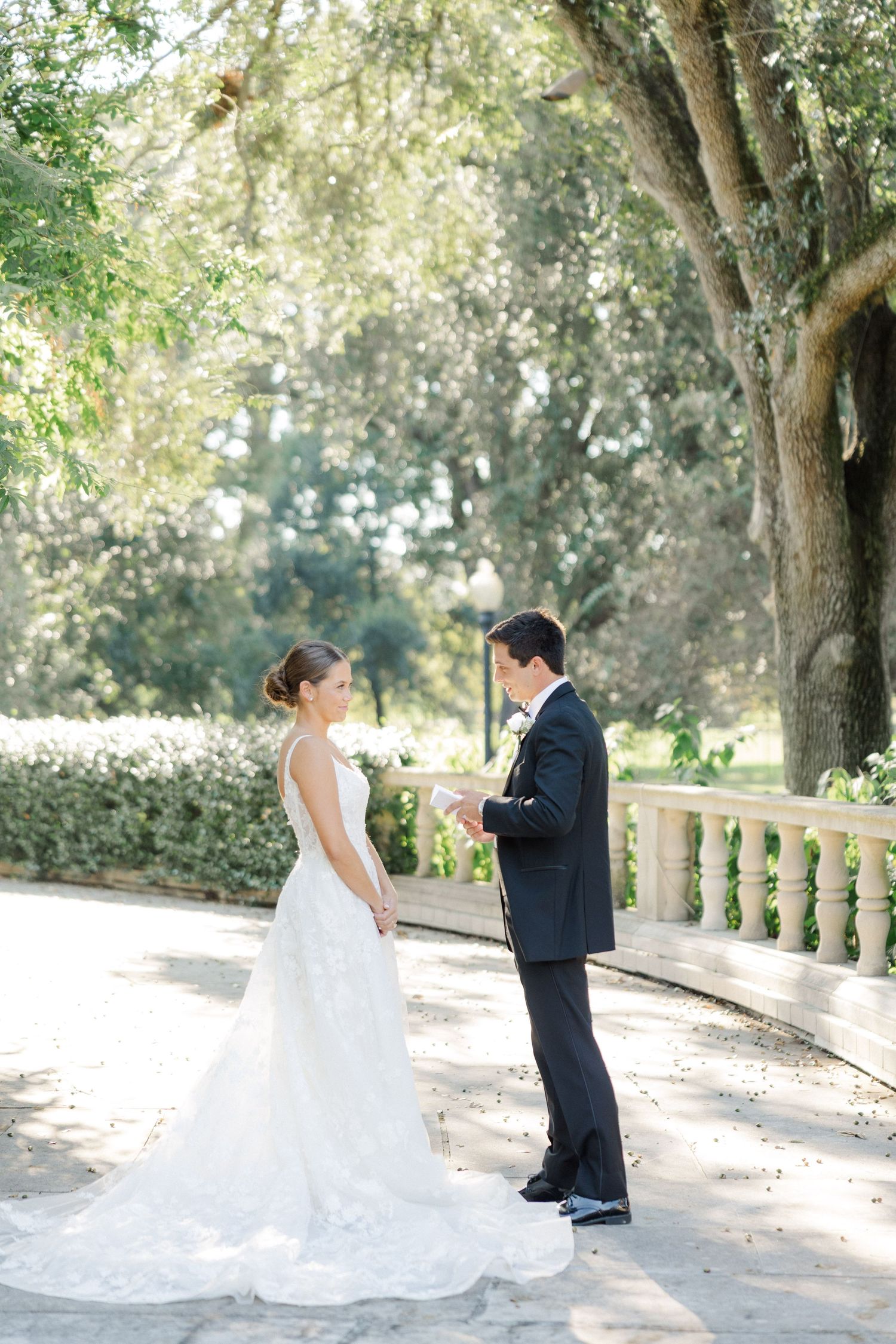Romantic wedding couple posing along a tree-lined path with white stone balustrades.