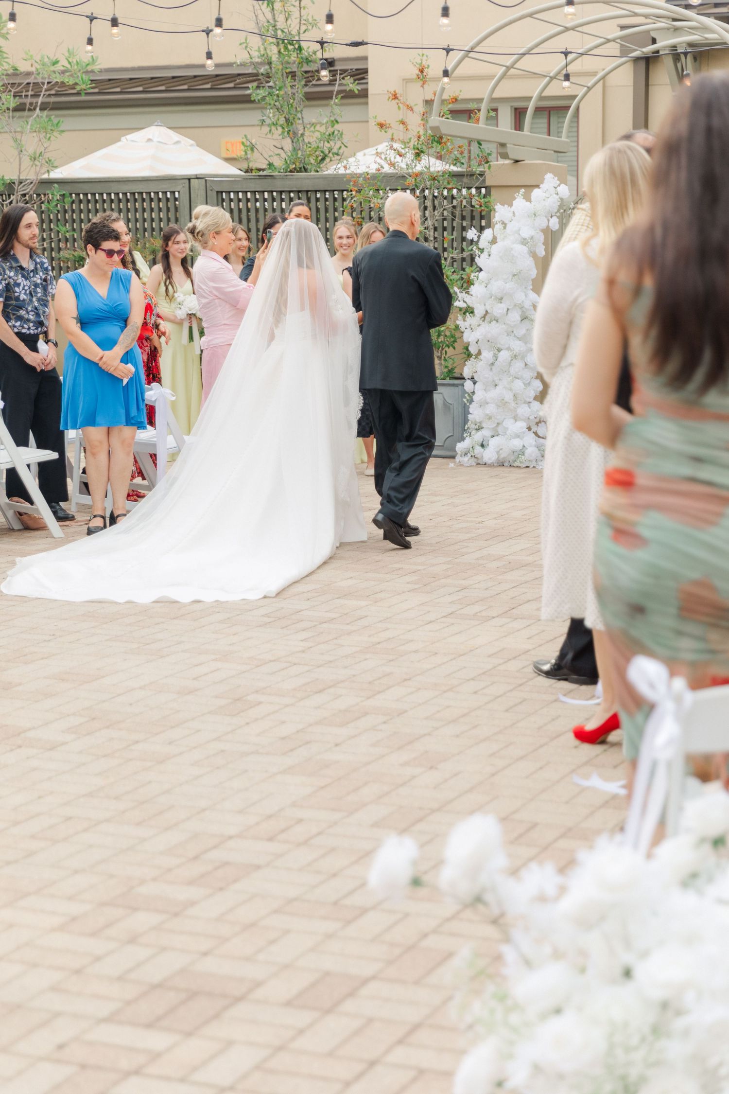 Outdoor wedding ceremony setup with string lights and guests gathering on stone patio.