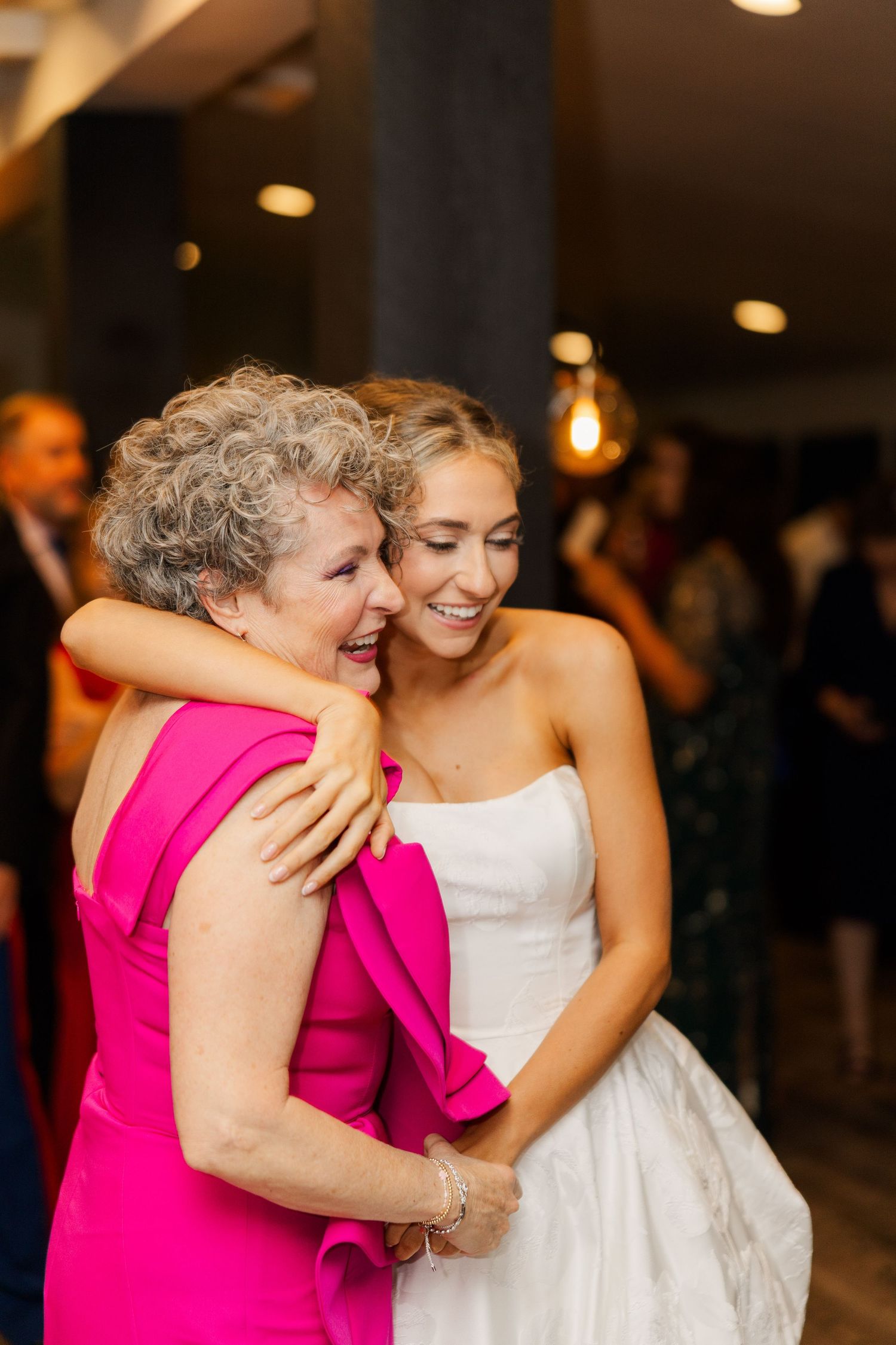 Emotional embrace between a woman in bright pink and a bride in a white wedding gown.