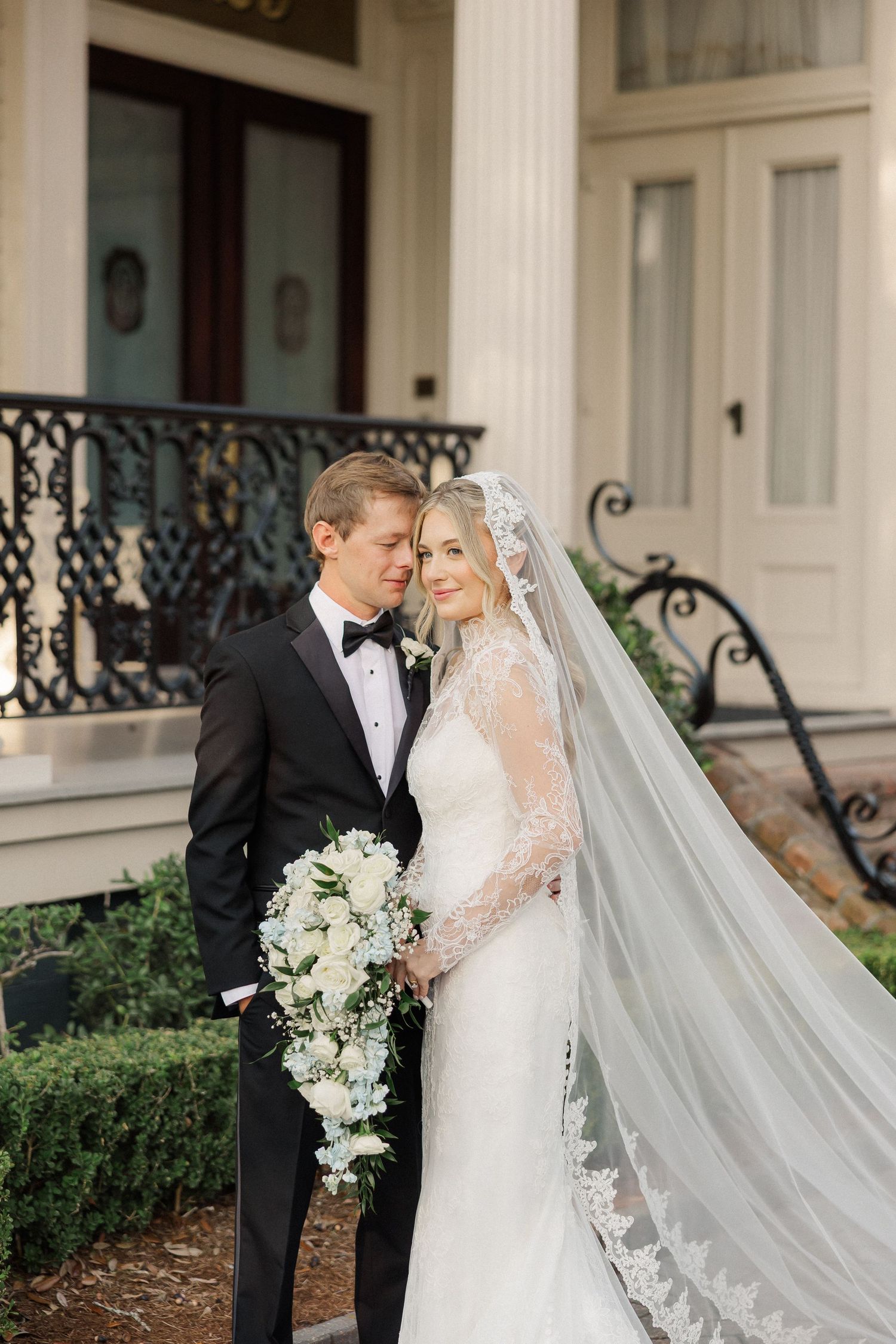 Elegant wedding portrait in front of a historic building with ornate ironwork and cascading bouquet.