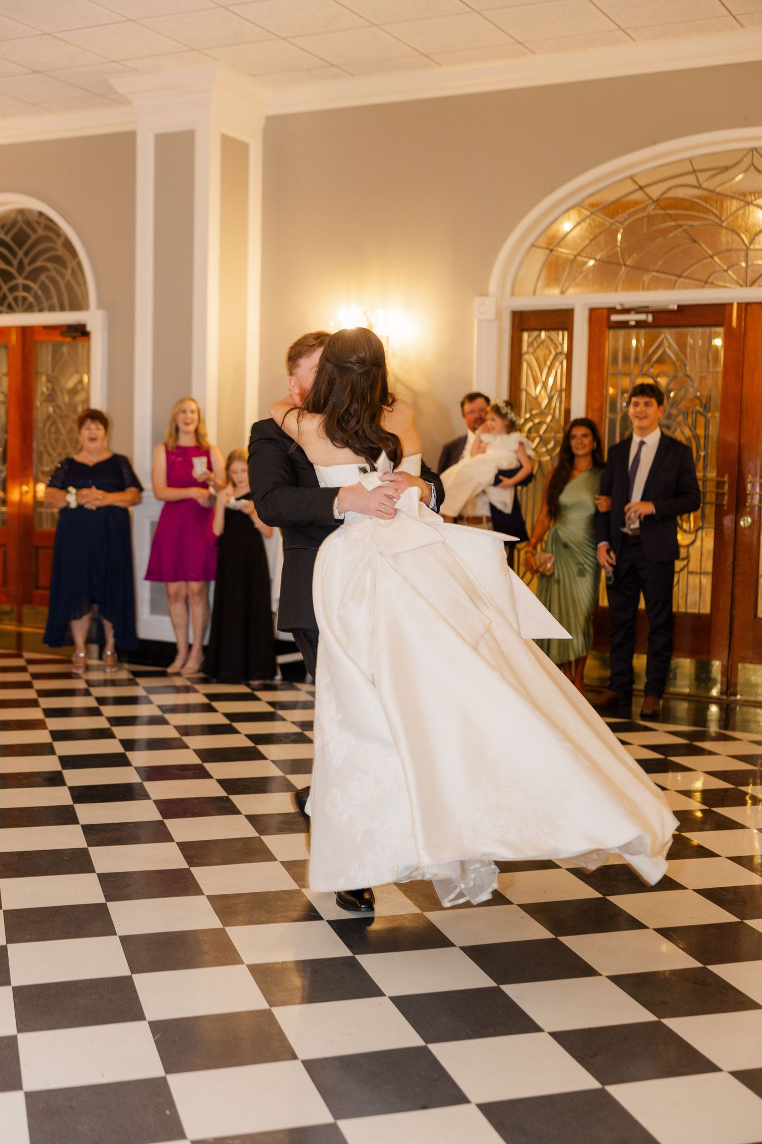 Wedding guests watch a couple dance on a black and white checkered ballroom floor.