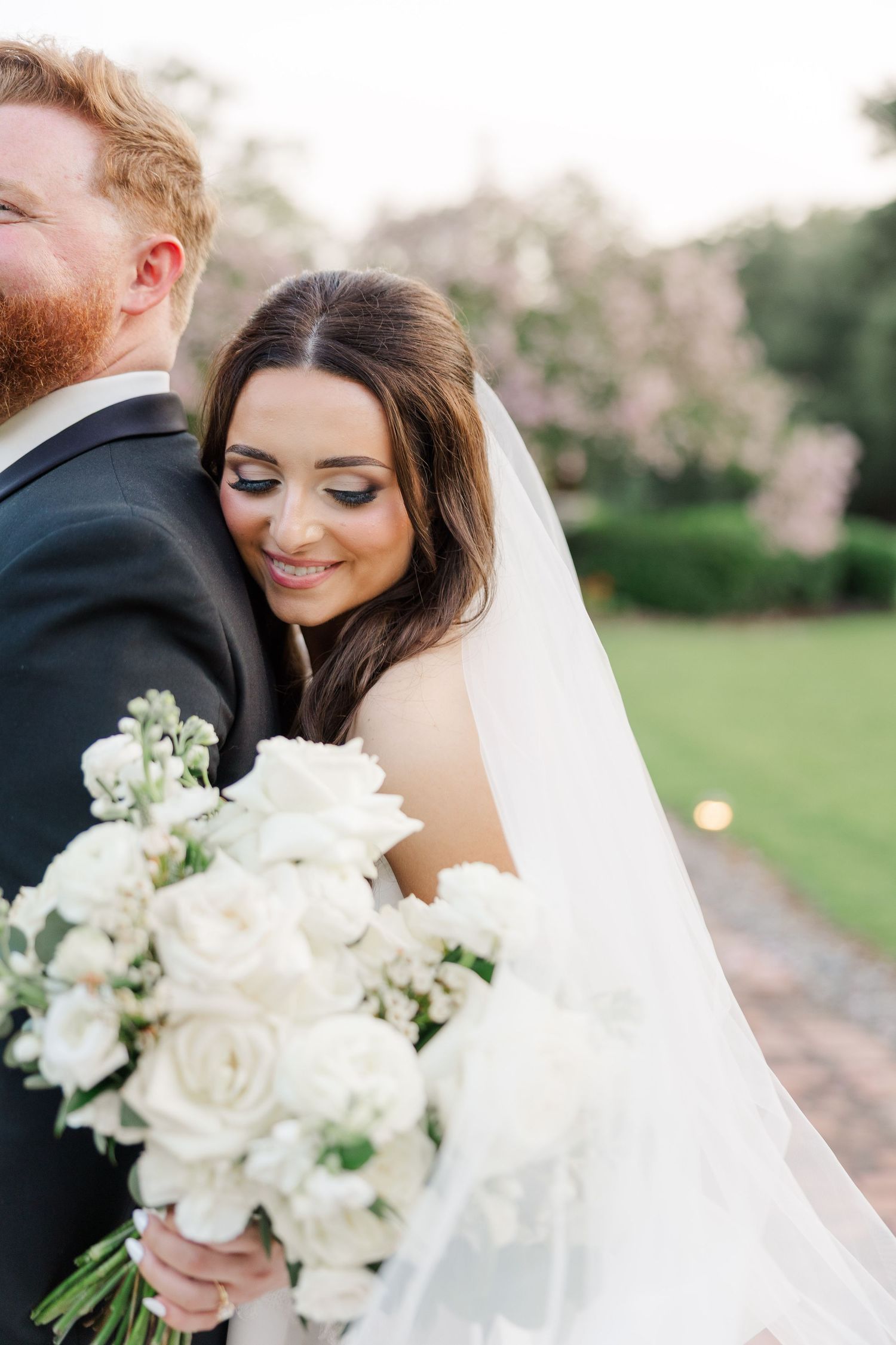Romantic outdoor wedding photos with bride holding white bouquet and groom in black suit.