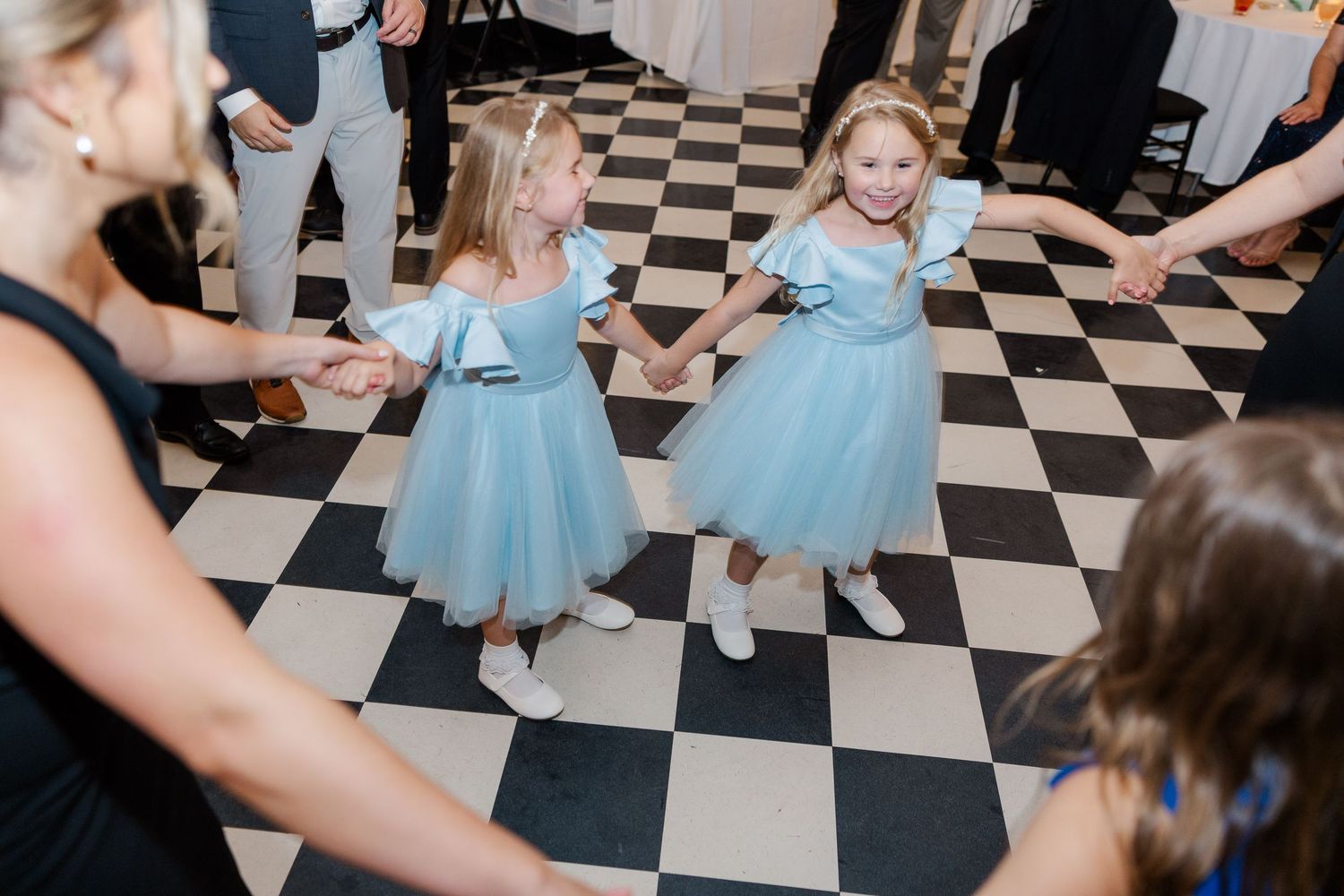 Wedding guests dancing on black and white checkered floor in formal attire.