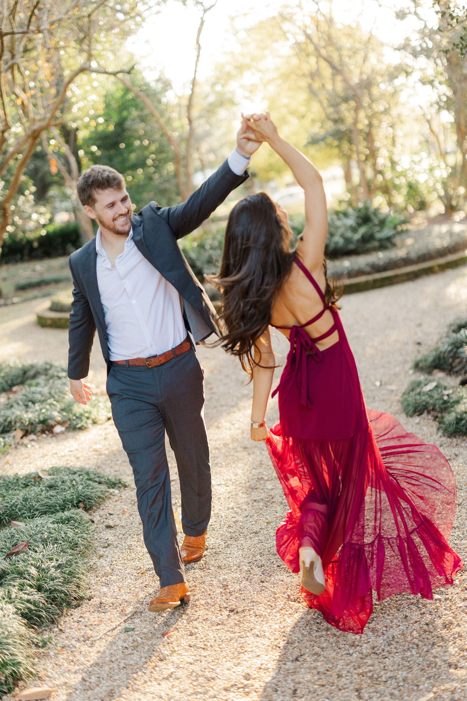 Playful couple dances and spins together on leaf-covered garden path during sunset.