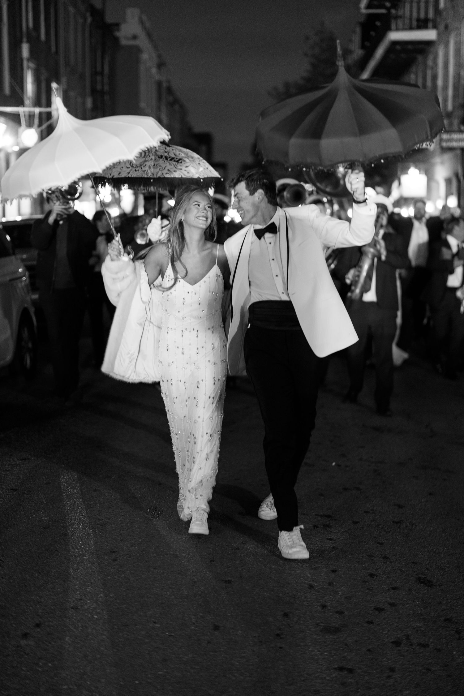 Black and white photo of couple walking under umbrellas at night.