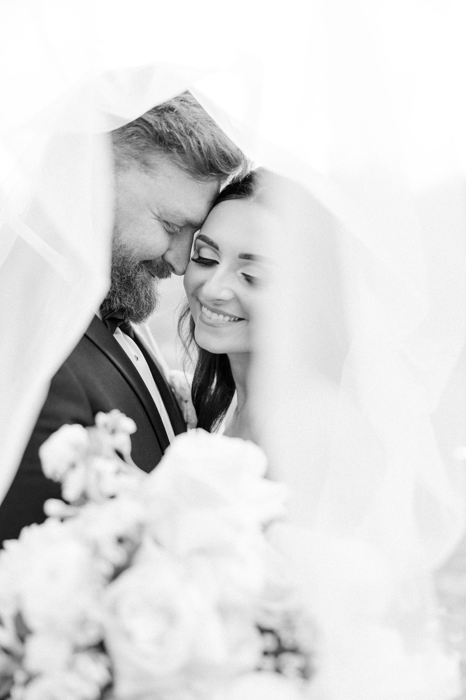 Black and white romantic wedding photography with soft bokeh flowers in foreground creating dreamy atmosphere.
